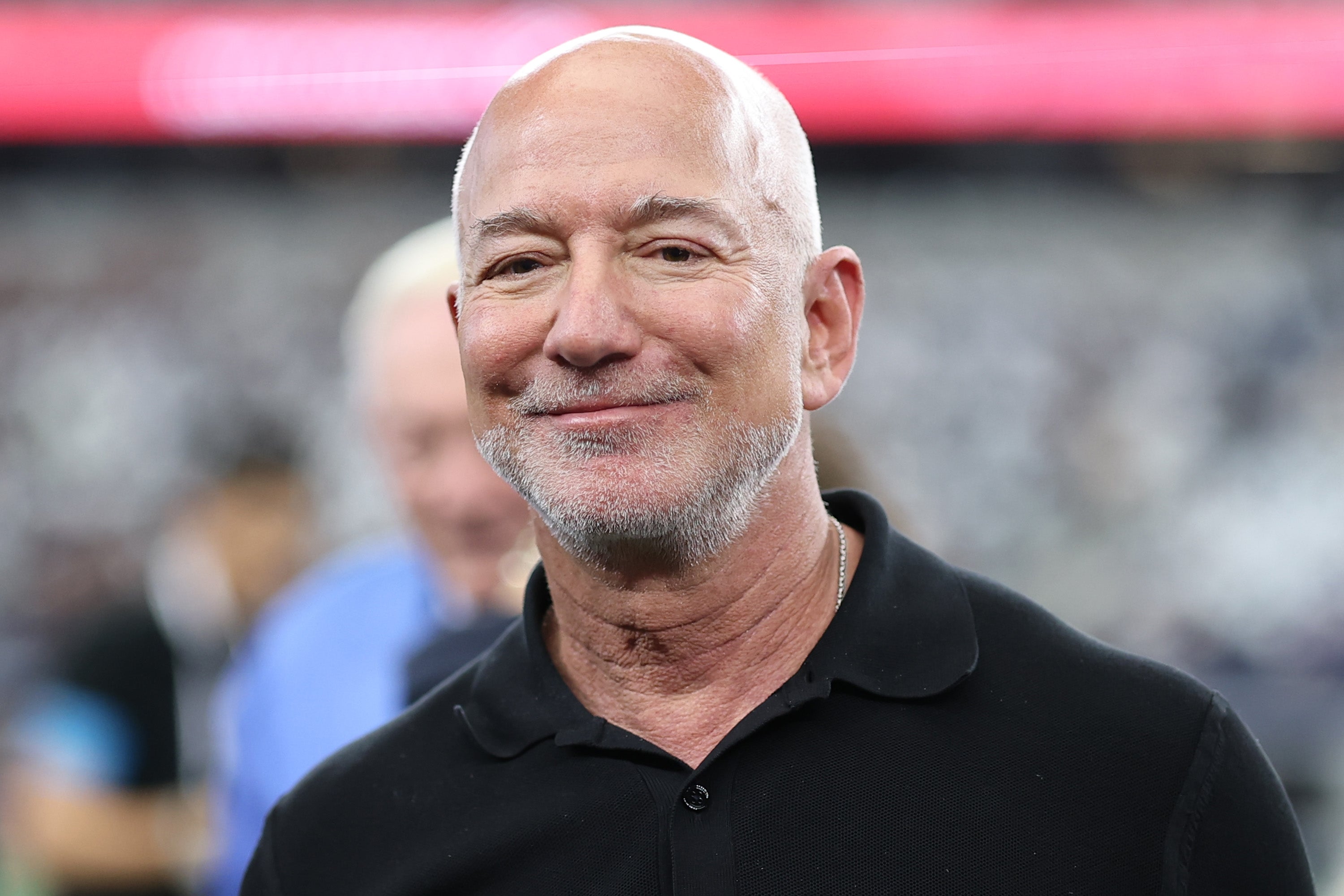 A person with a short beard, smiling, wearing a casual polo shirt in a busy setting
