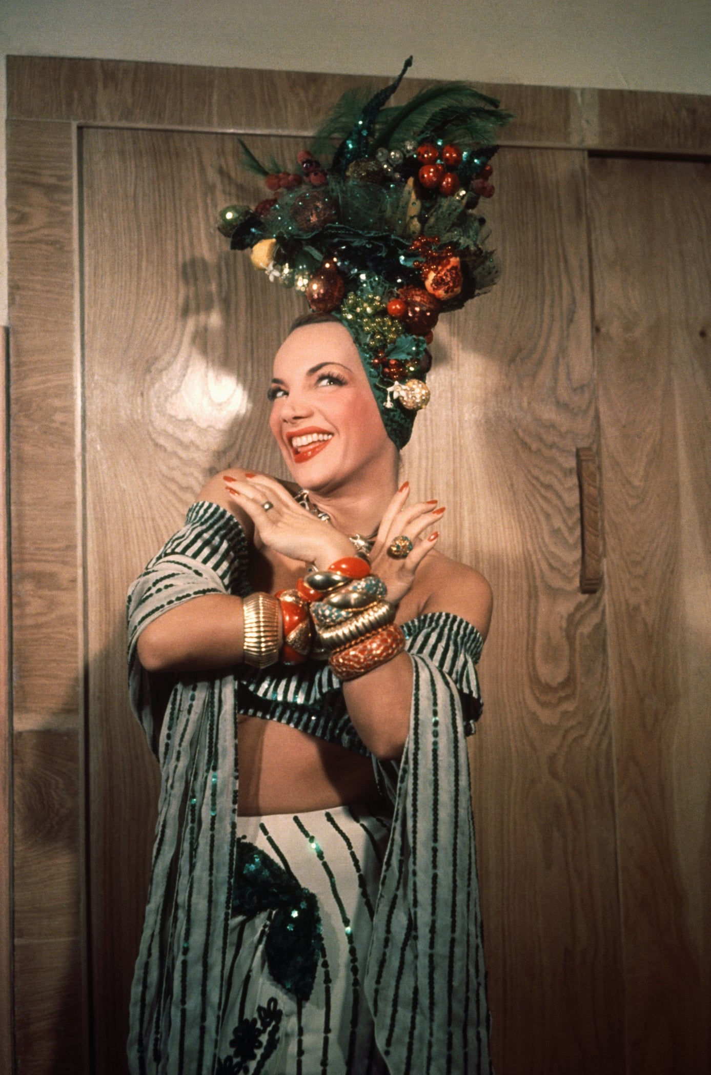 Person in a vibrant, tropical-themed outfit with fruit-inspired headpiece, smiling and posing with arms crossed