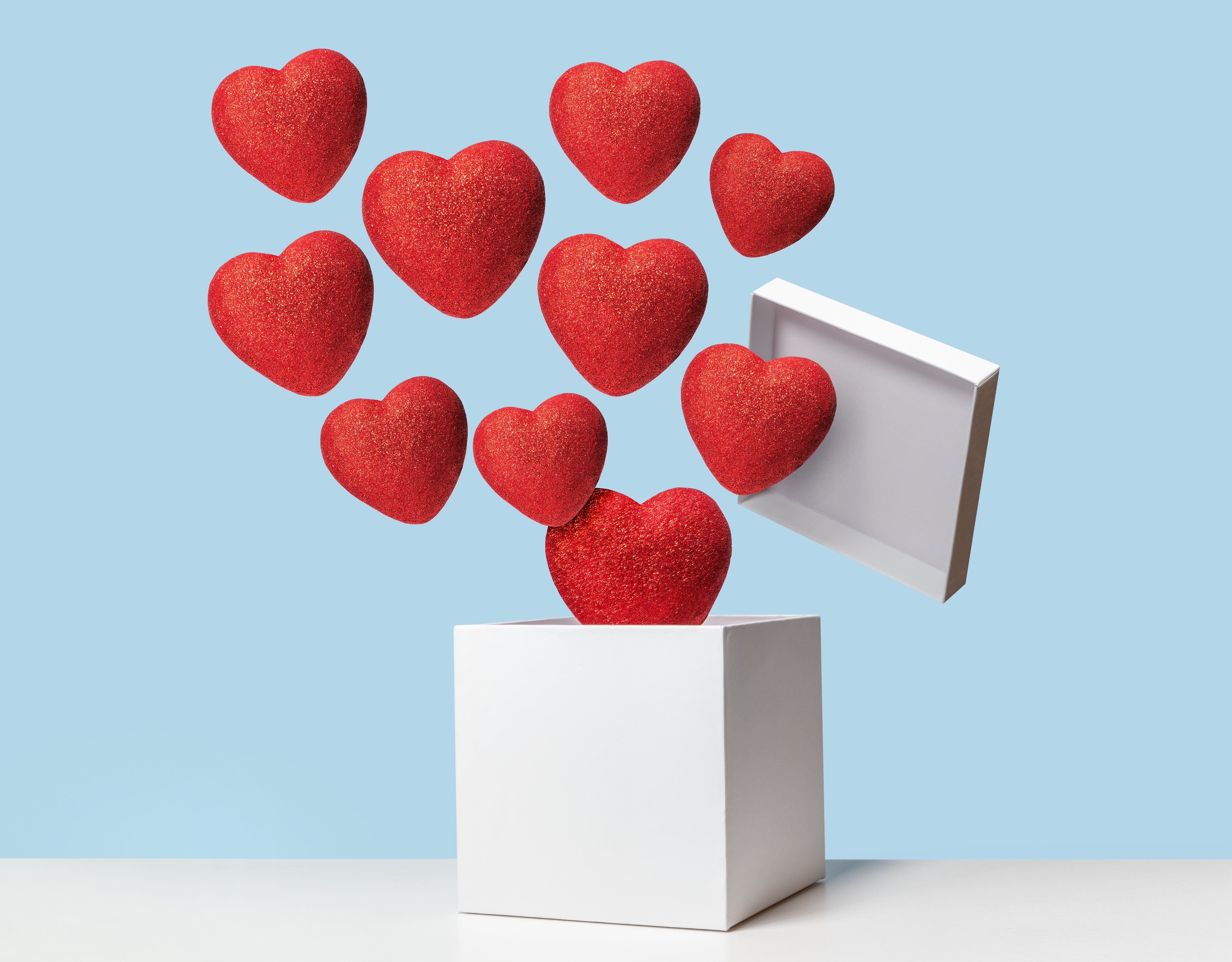 Floating red hearts emerging from an open white box against a plain background, symbolizing love or heart health
