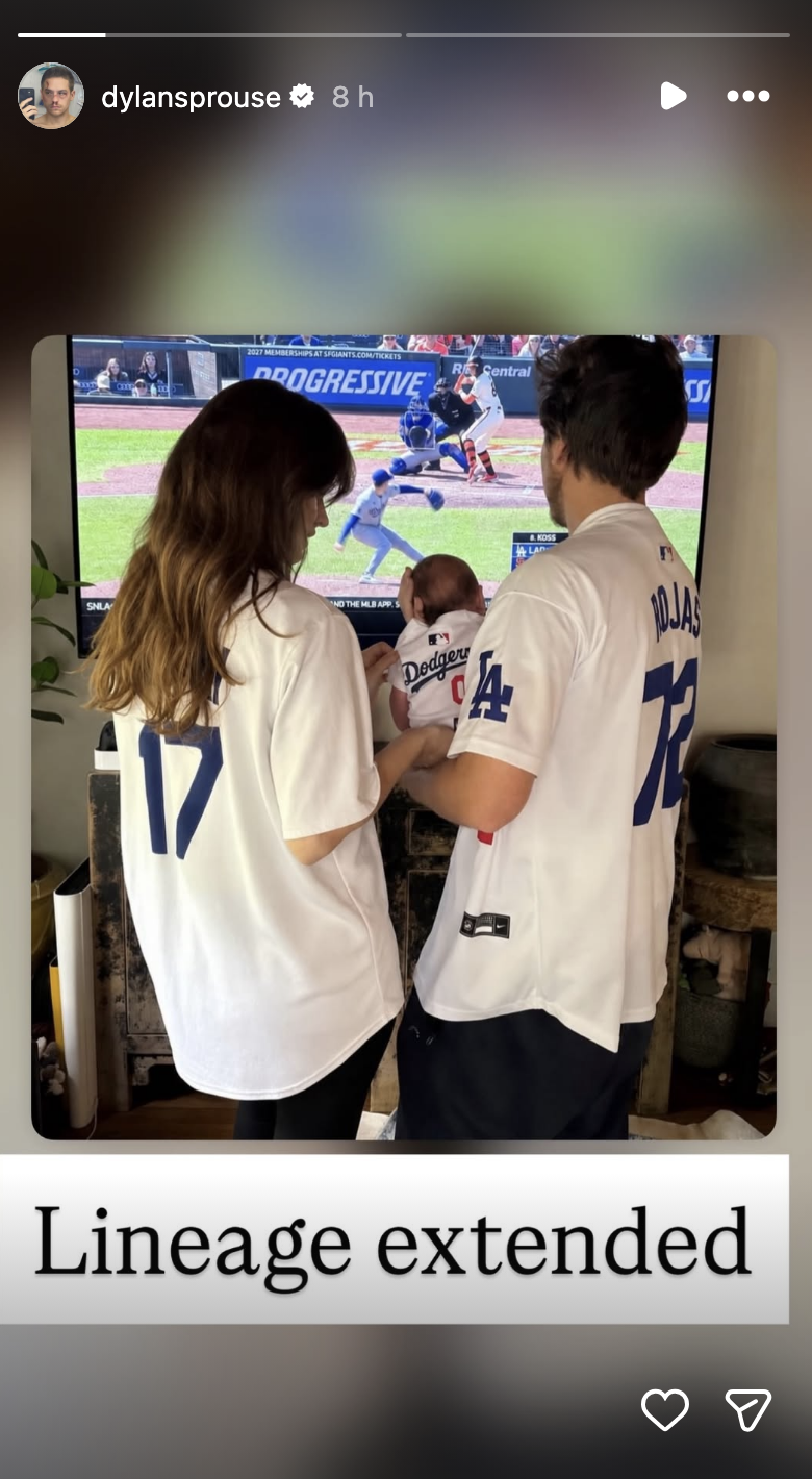 Two adults in baseball jerseys hold a baby in a Dodgers outfit, standing in front of a TV displaying a baseball game. Text: "Lineage extended."