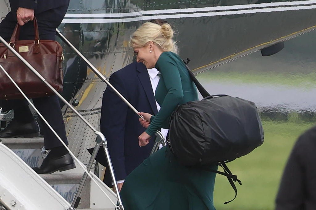 Person i lang kjole går om bord i et fly med en stor bag, ledsaget av andre som bærer bagasje