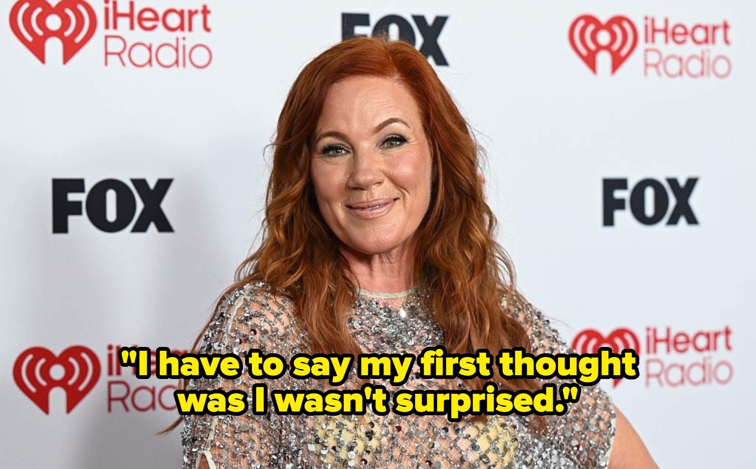 Woman in glittering sheer top smiles at iHeartRadio event backdrop with logos