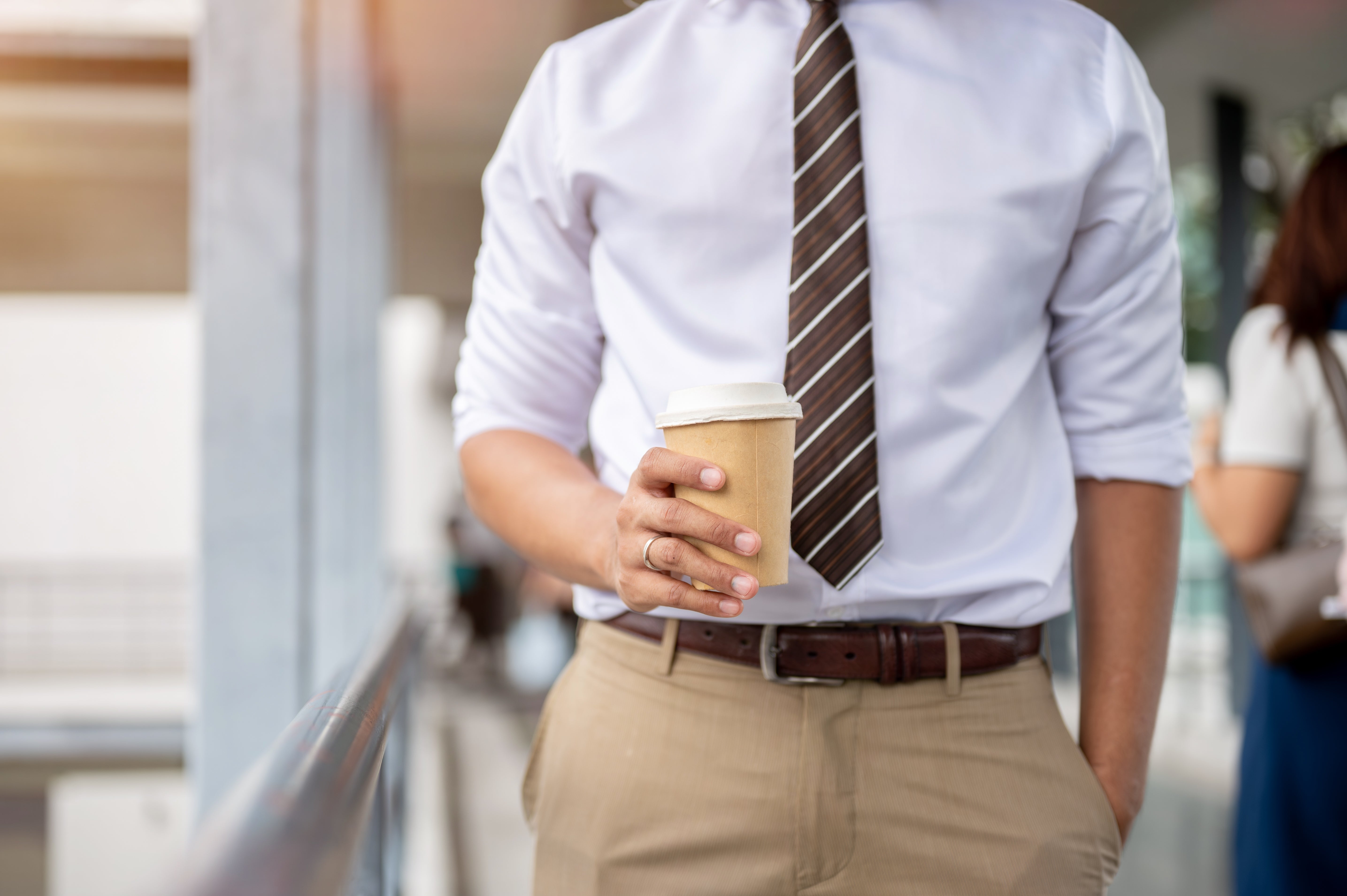 Mann i hvit skjorte og stripet slips som holder en kaffekopp, står uformell med en hånd i lommen