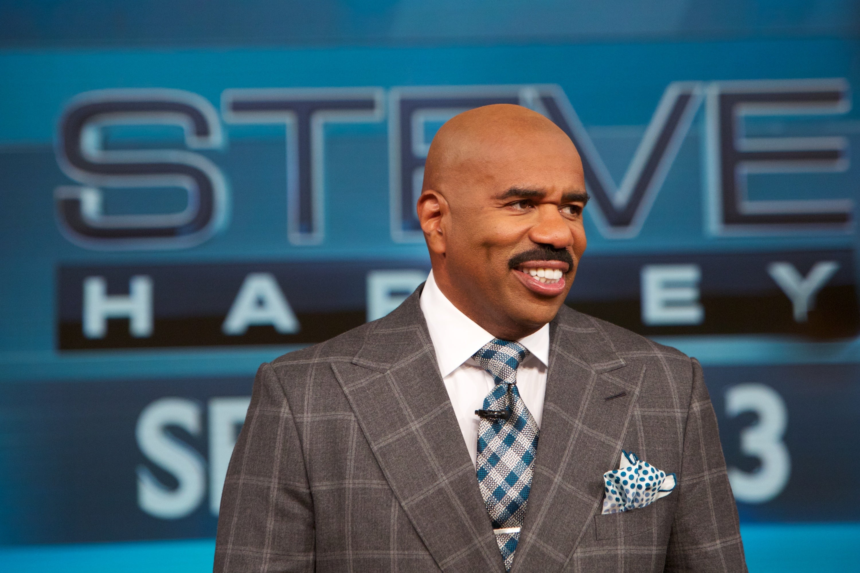 Mann i rutete dress og mønstret slips står foran store "Steve Harvey" skilt