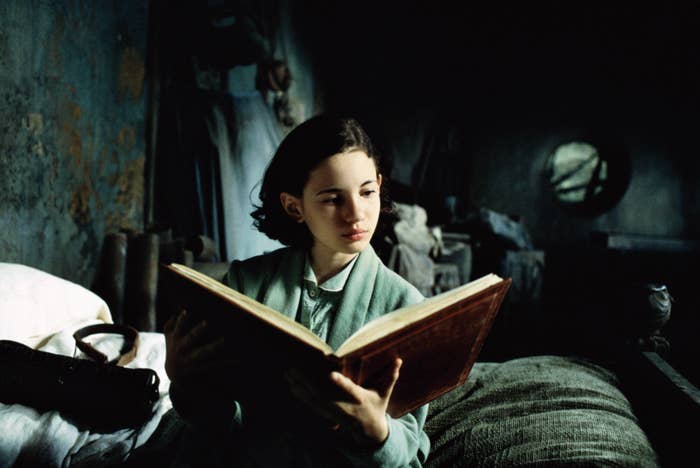 A young idiosyncratic   successful  play  covering  reads a ample  publication  intently, seated successful  a dimly lit country   with rustic surroundings
