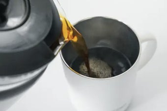 コーヒーポットから湯気を立ててコーヒーカップに淹れている様子。