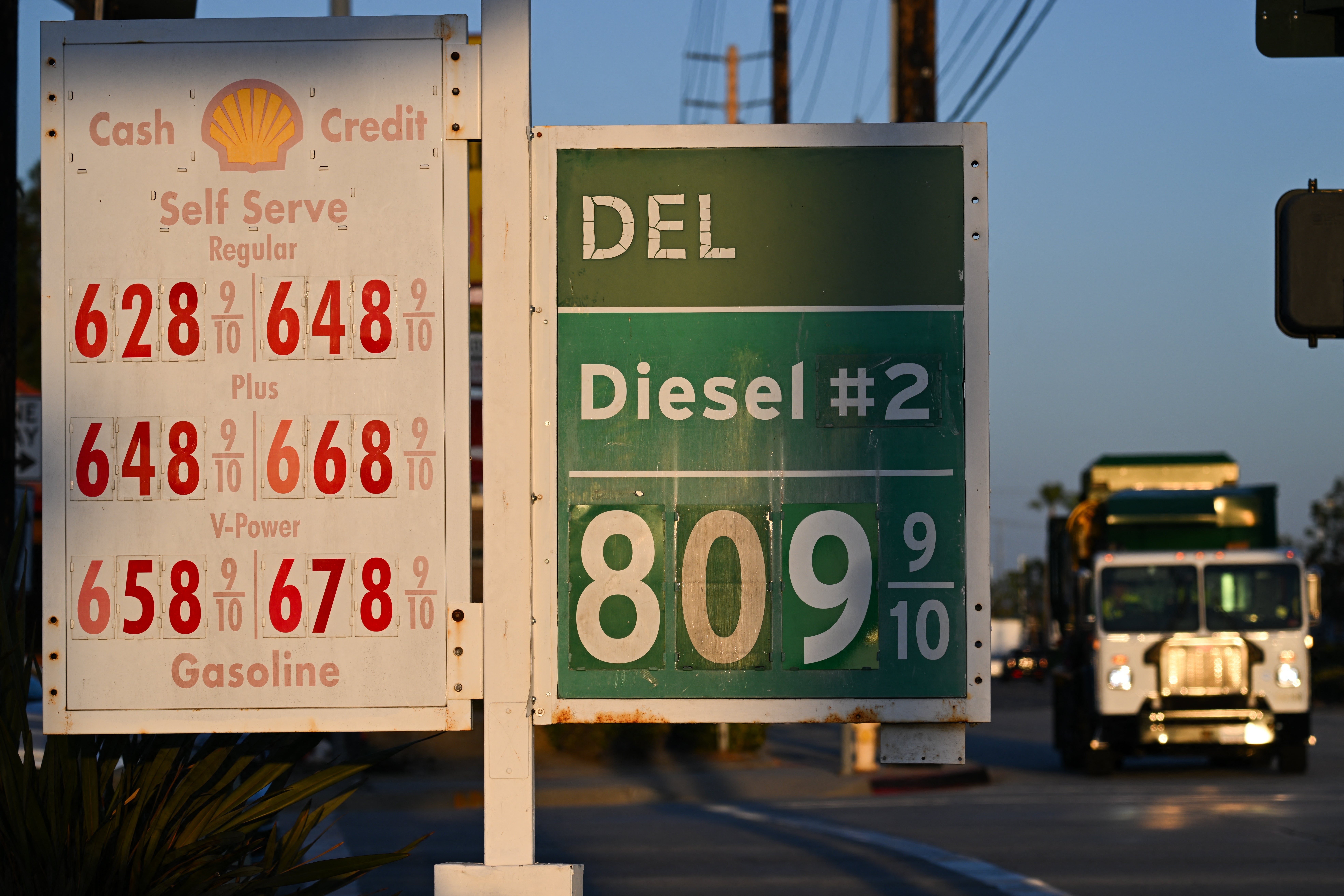 Bensinstasjonsskilt som viser priser: Vanlige $6,28-$6,48, pluss $6,48-$6,68, V-Power $6,58-$6,78, Diesel $8,09. Lastebil i bakgrunnen