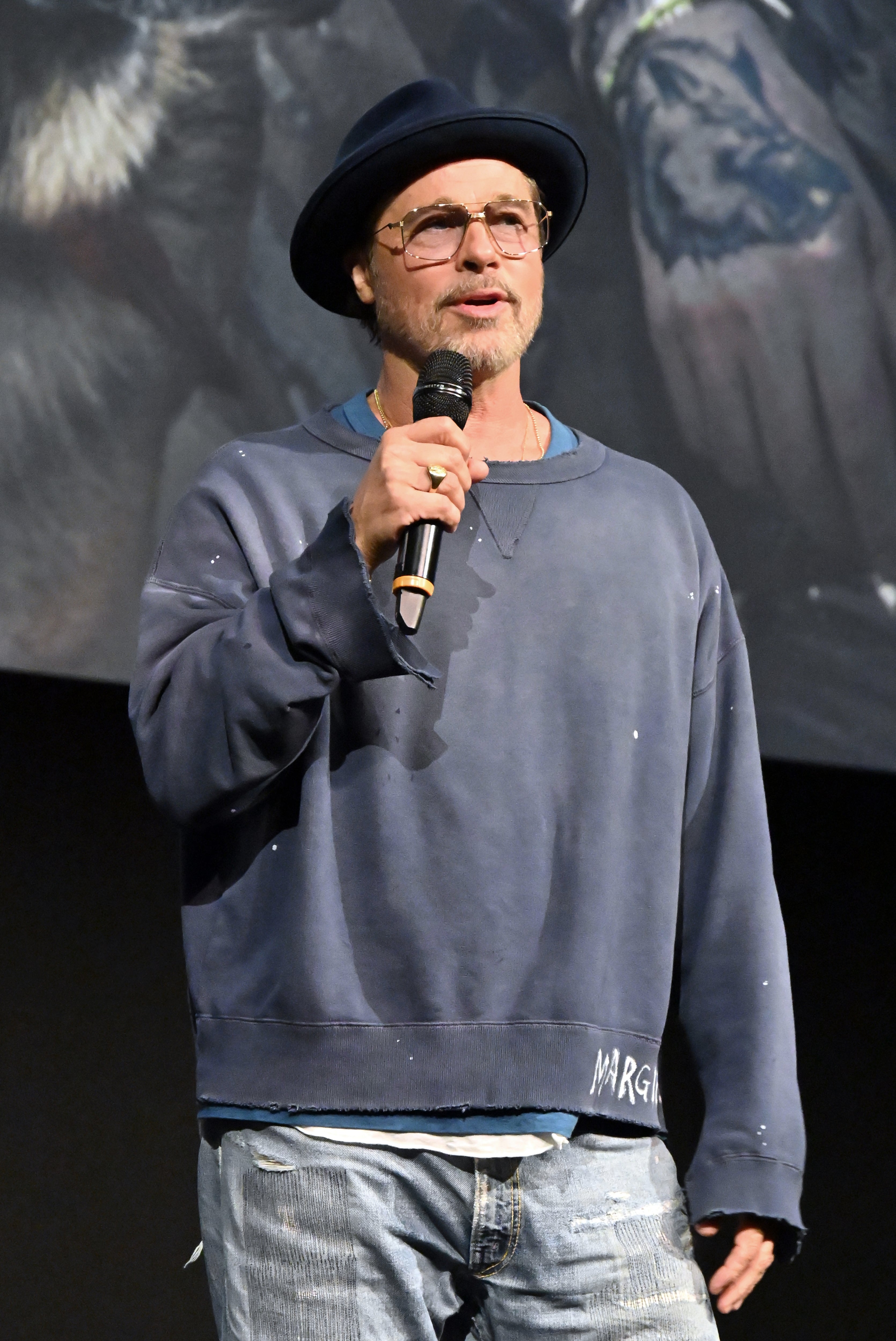 Man wearing a casual hat and oversized sweatshirt holds a microphone on stage