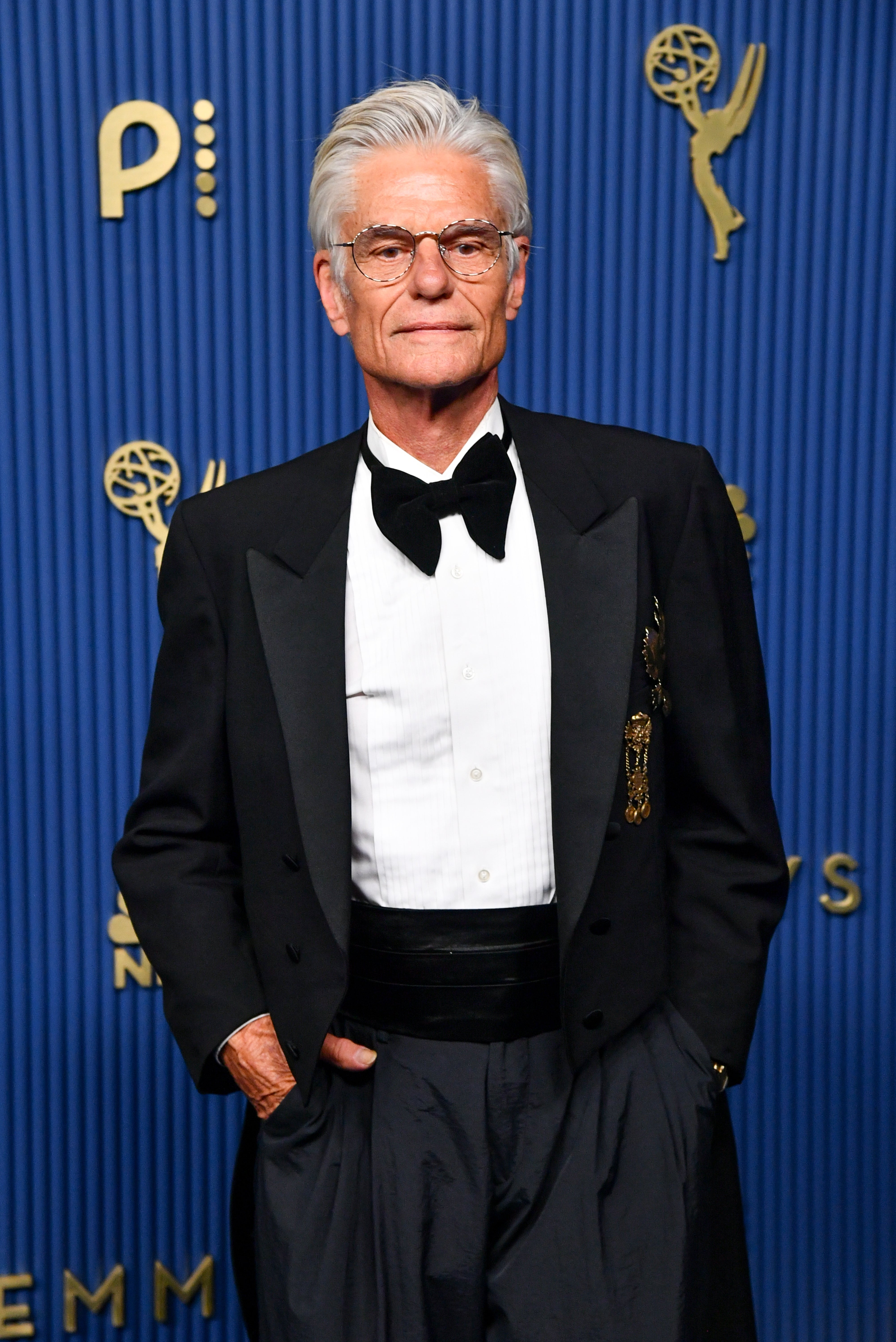 Person in a formal black tuxedo and bow tie on a red carpet, posing confidently