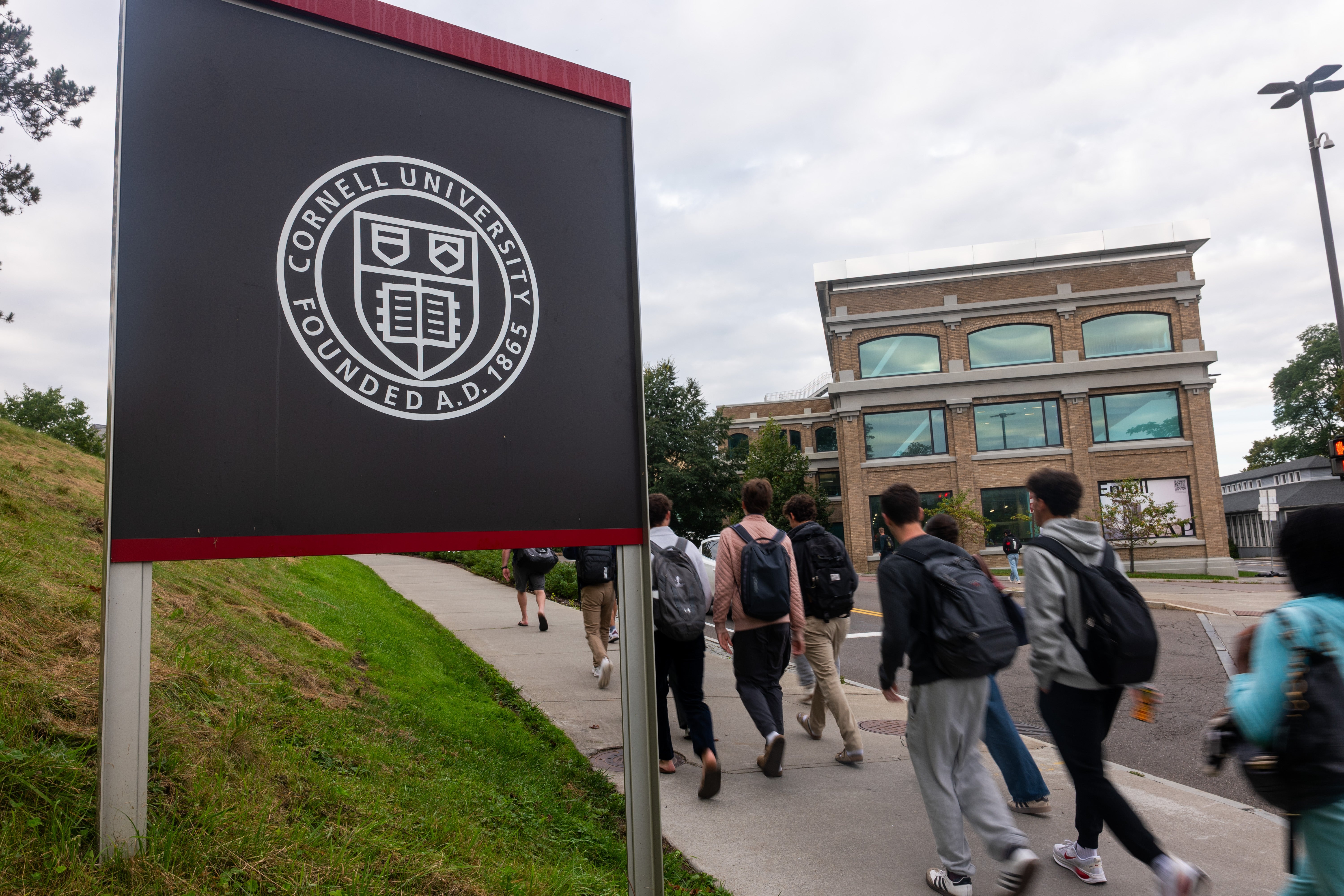 Folk som går forbi et Cornell University-skilt på en campusvei mot en bygning