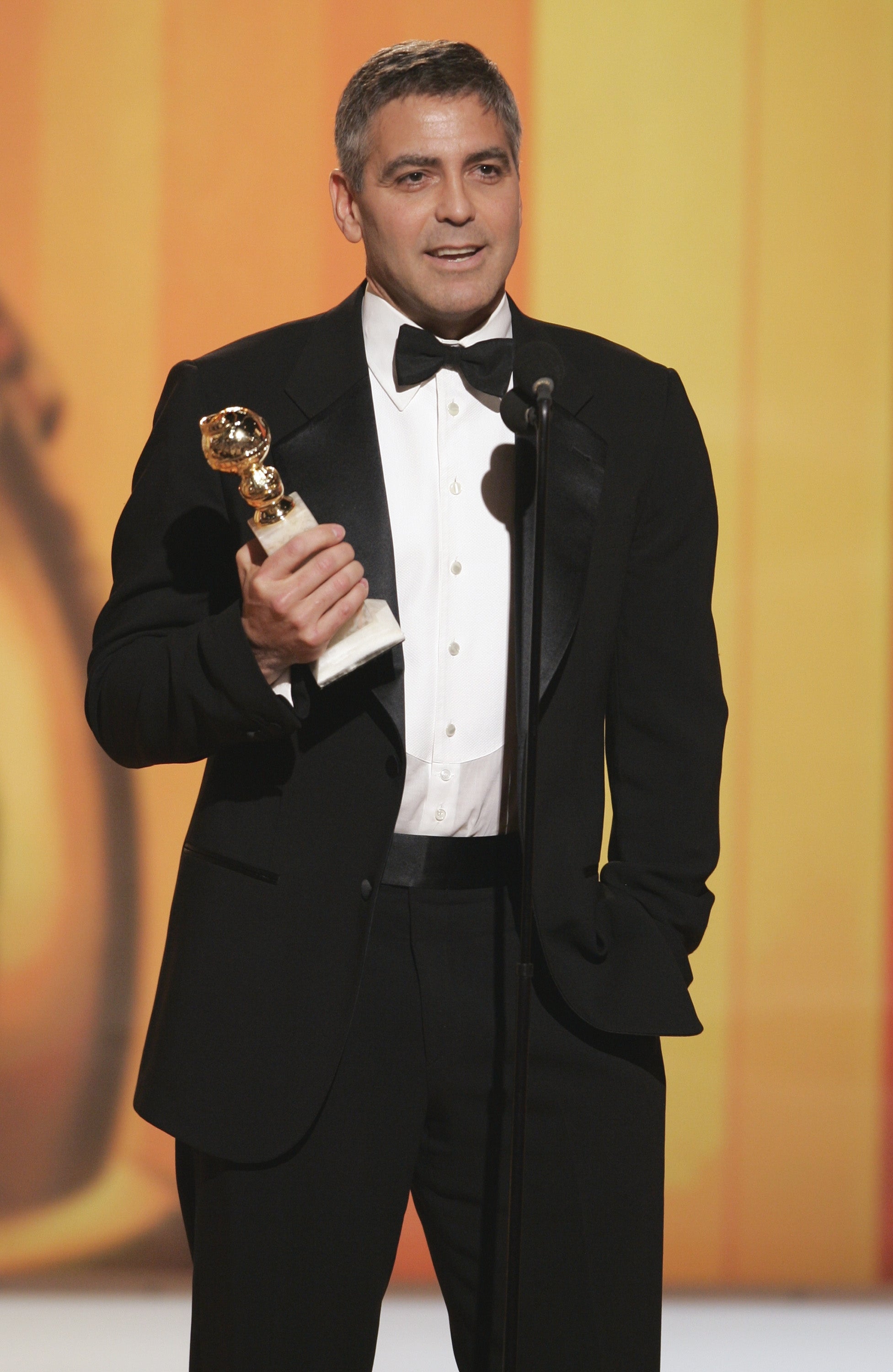 A person onstage in a tuxedo holds an award, possibly at a formal event or ceremony