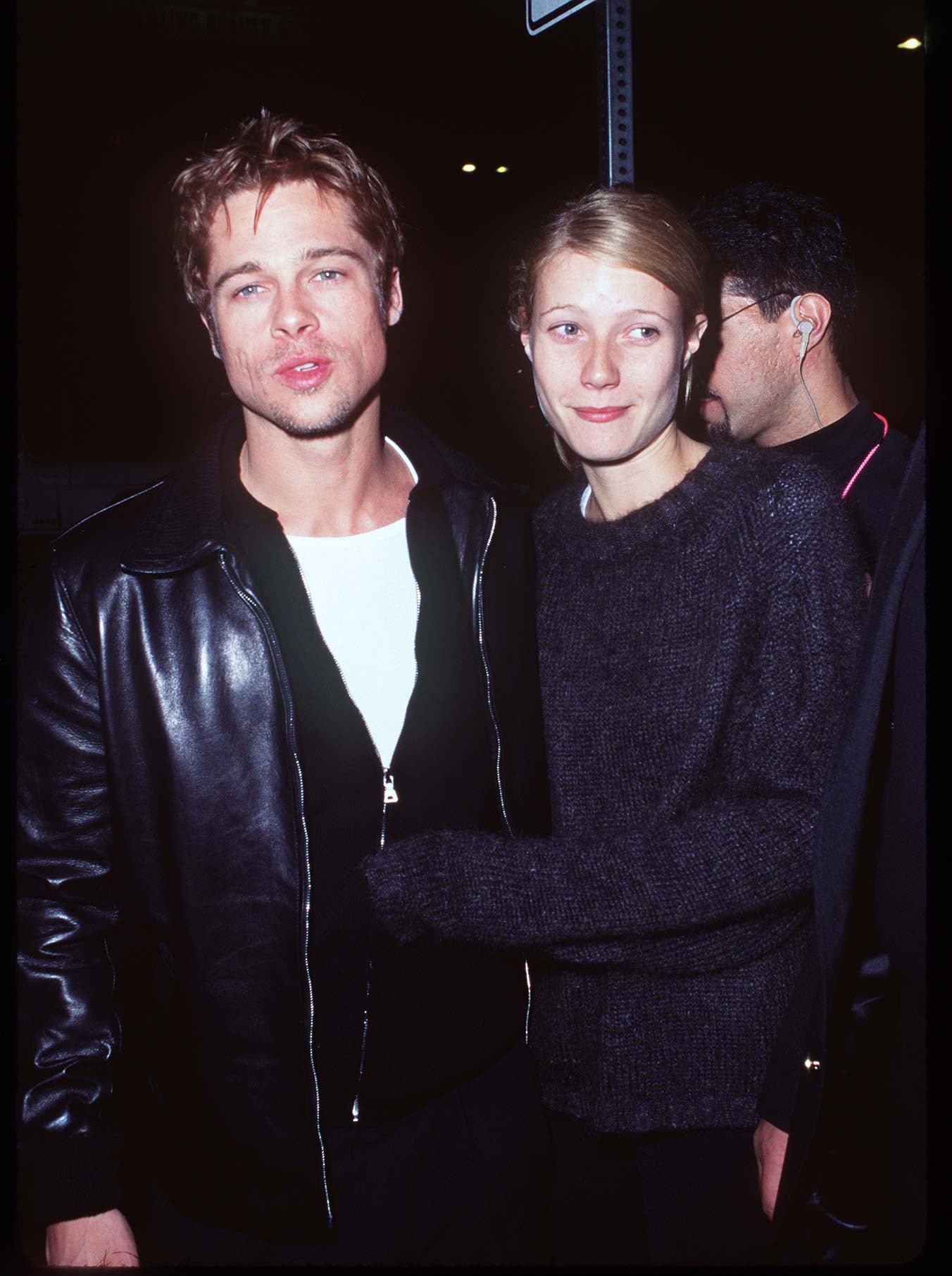 A couple poses on the red carpet; the man wears a leather jacket, and the woman wears a casual sweater