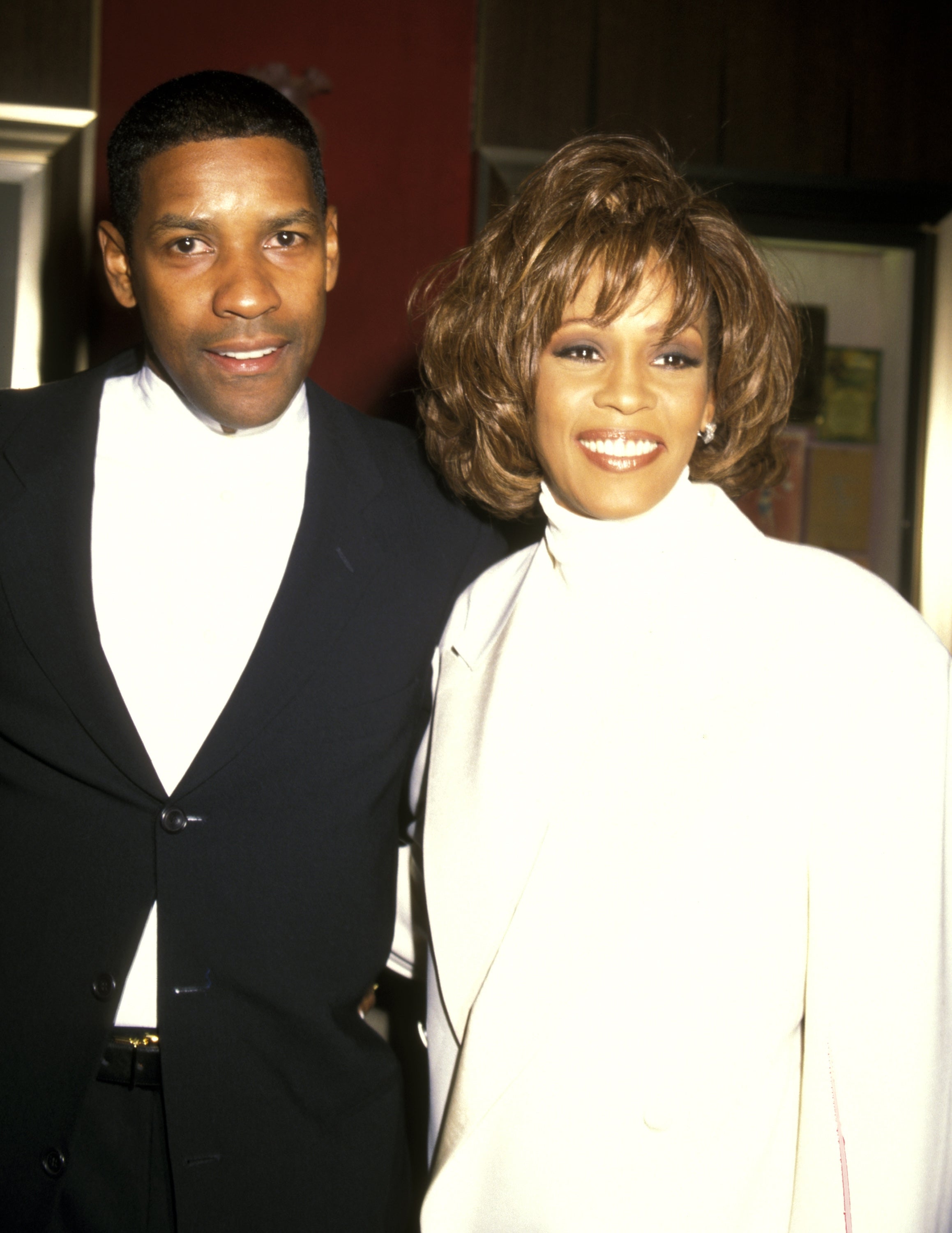 Two well-dressed celebrities pose together, smiling, wearing elegant outfits at an event