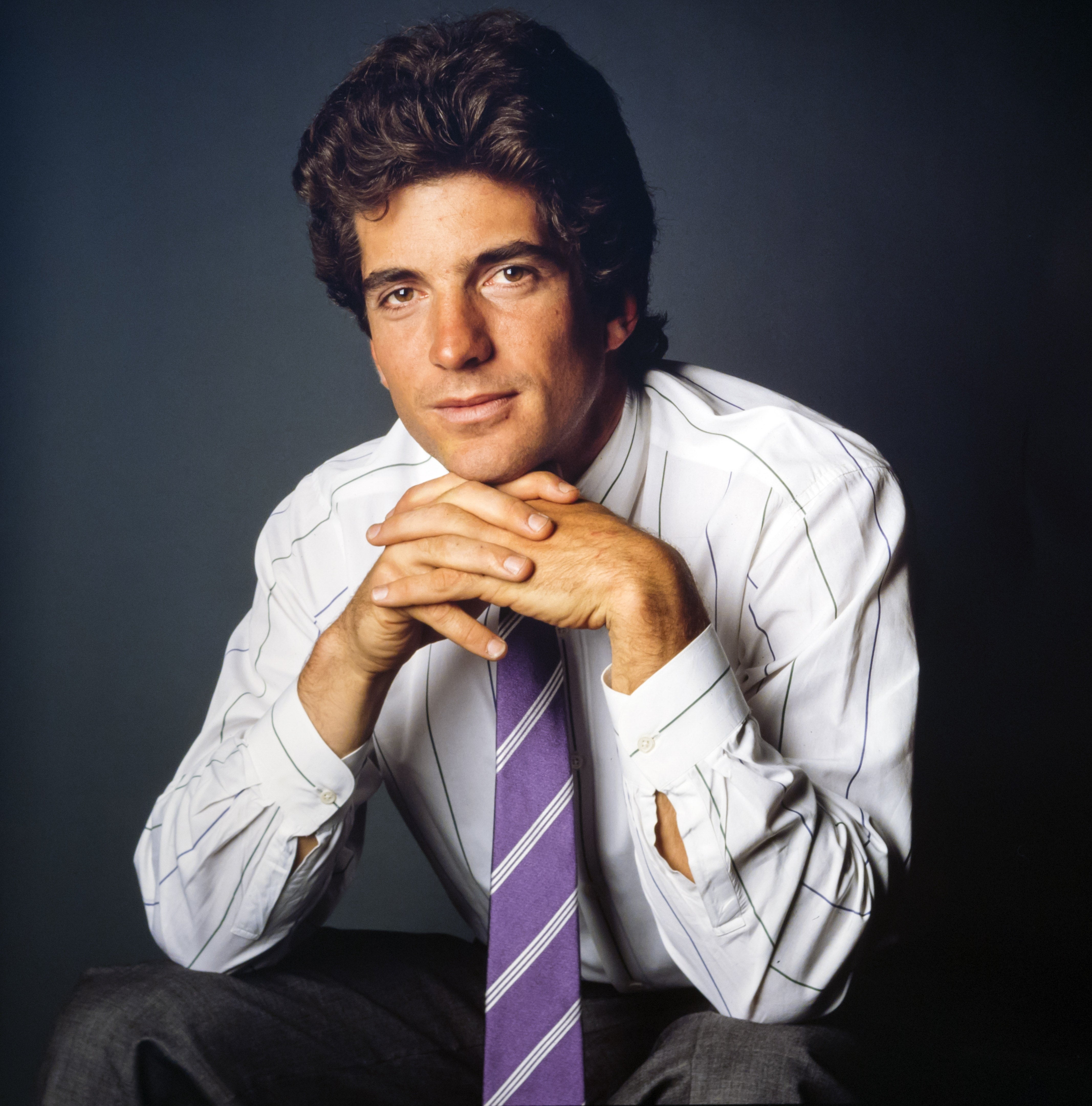 Person in a striped dress shirt and tie, posing with chin resting on hands