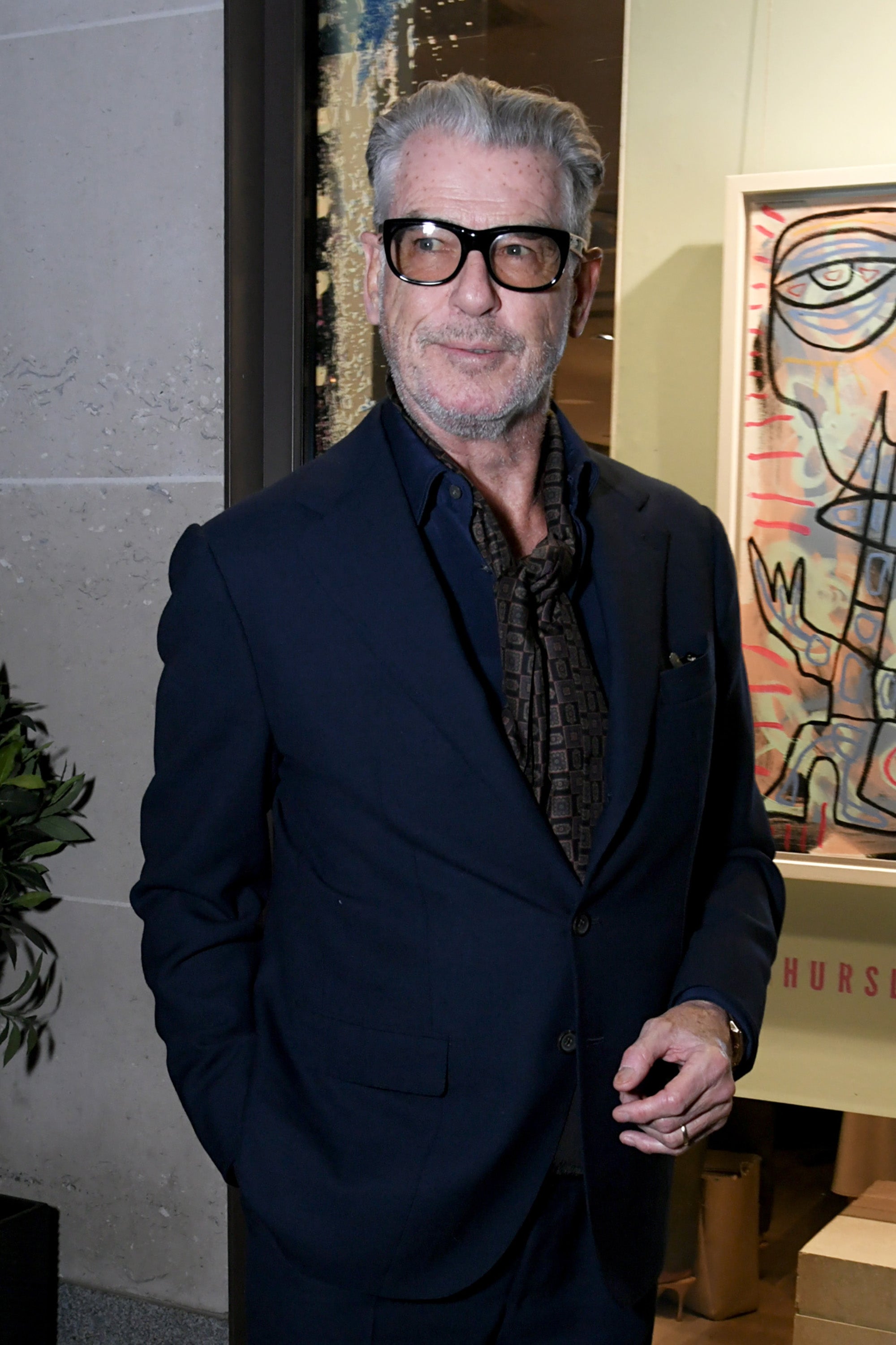 Person in a sleek suit with a patterned scarf stands at an event, exuding confidence and style