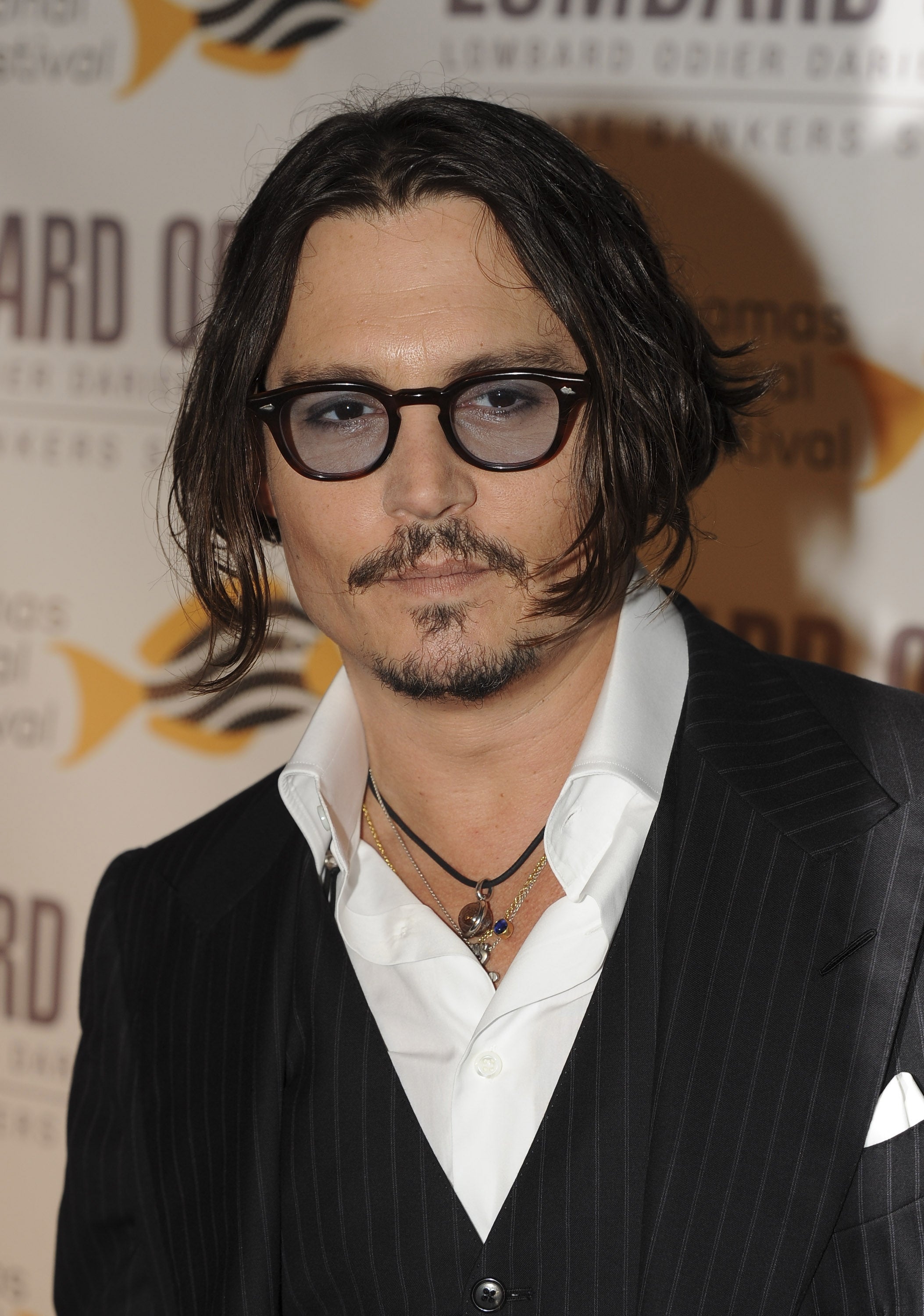 Person in pinstripe suit with layered necklaces and glasses at a formal event