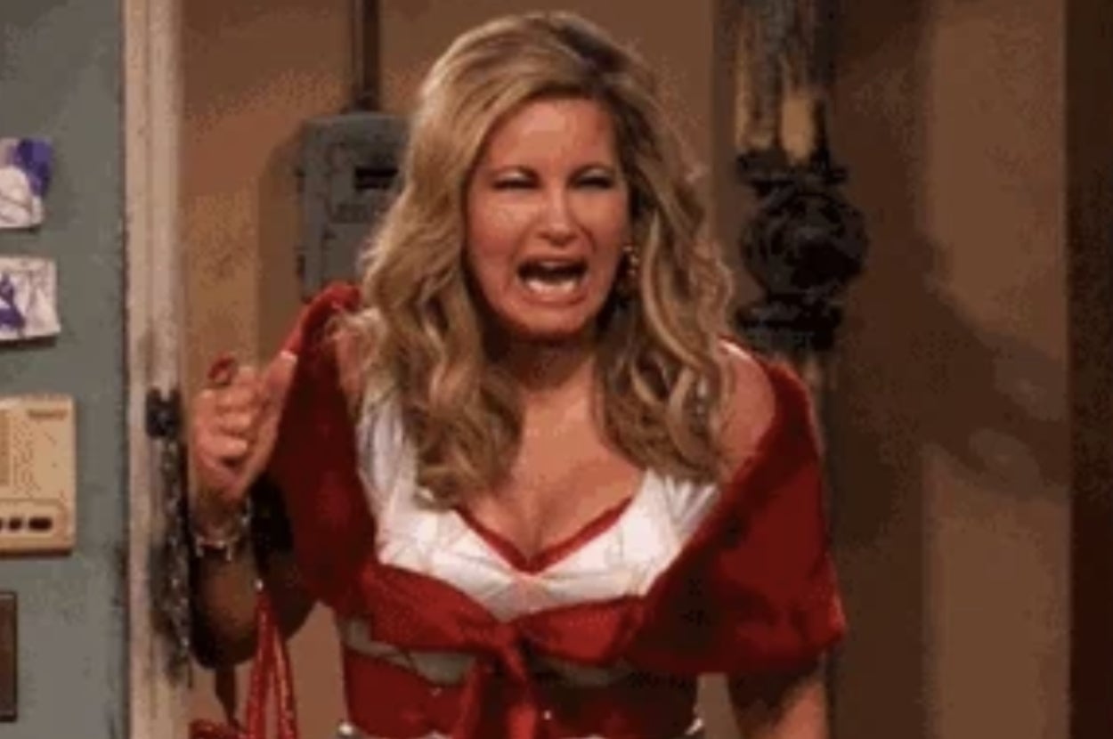 Person wearing a layered dress and holding a red bag, expressing excitement or surprise, standing indoors