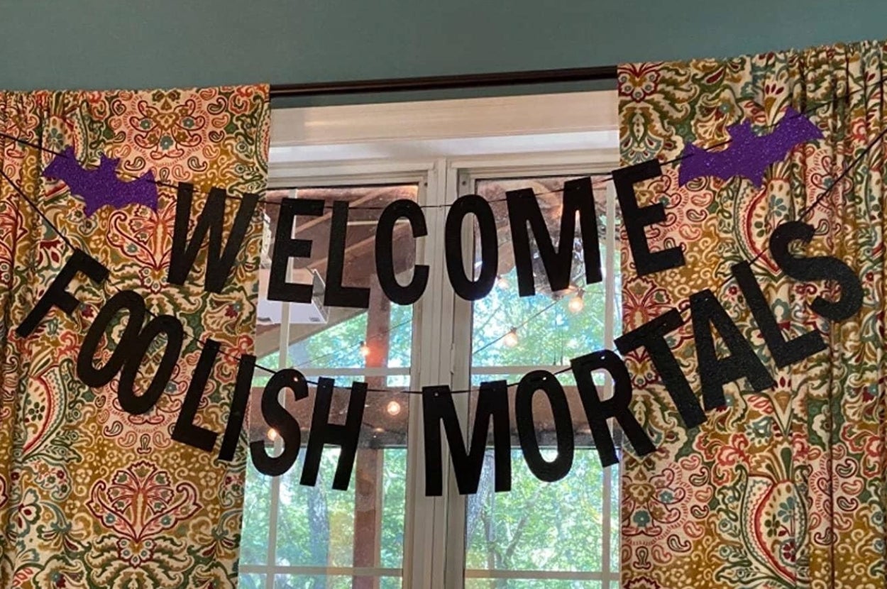 A Halloween banner with the text "Welcome Foolish Mortals" hangs in front of a window with patterned curtains