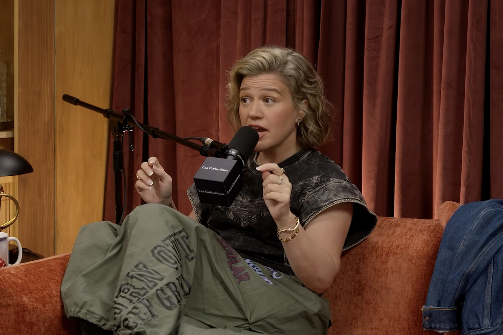 Person sitting on a sofa, speaking into a microphone during a podcast recording