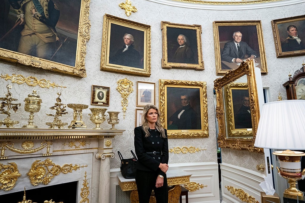 En person står i et utsmykket rom med gullaksenter, omgitt av portretter av historiske skikkelser