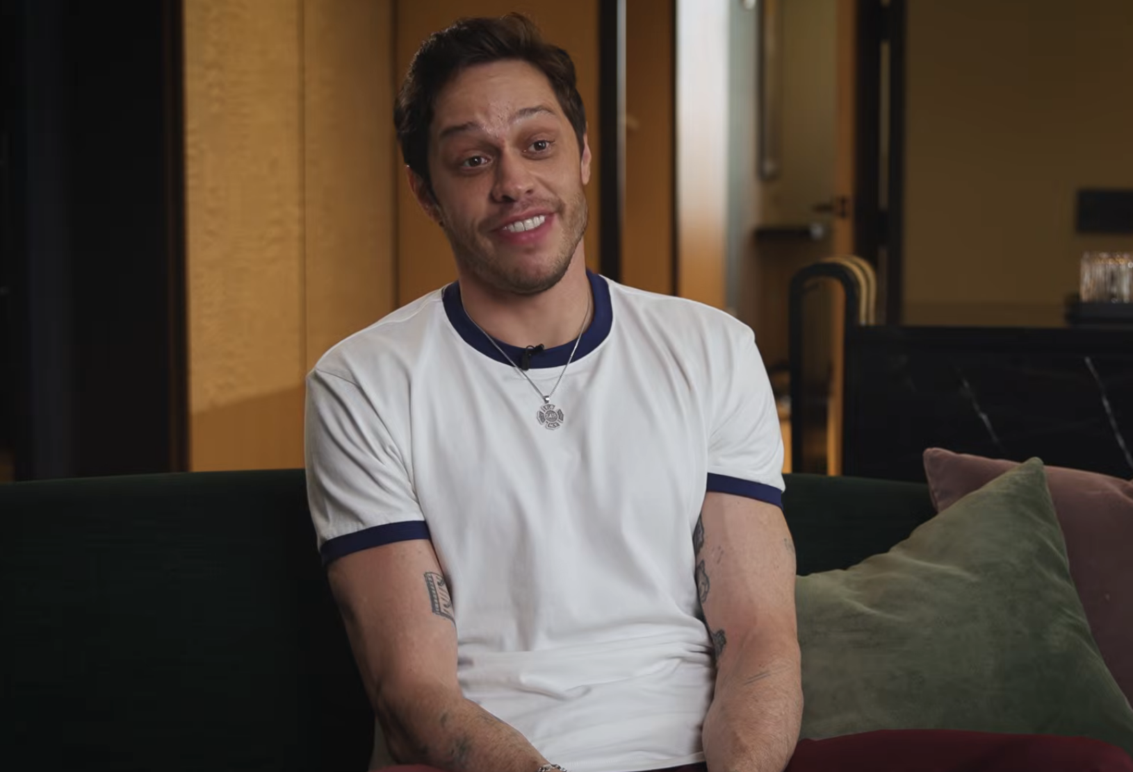 Person sitting on a couch, wearing a casual t-shirt and jewelry, smiling at the camera