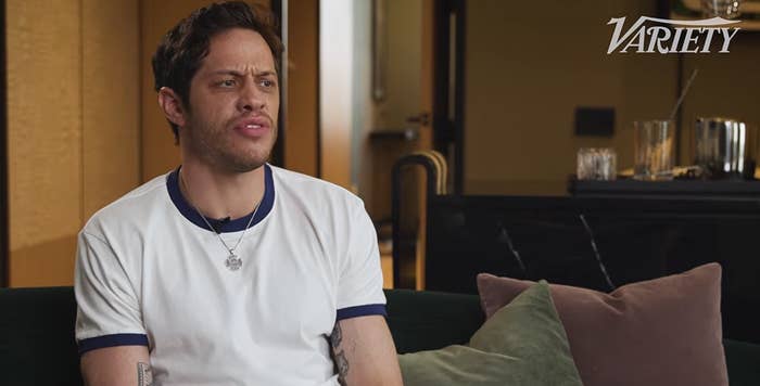Person in casual white shirt sitting on a couch during an interview, with a thoughtful expression