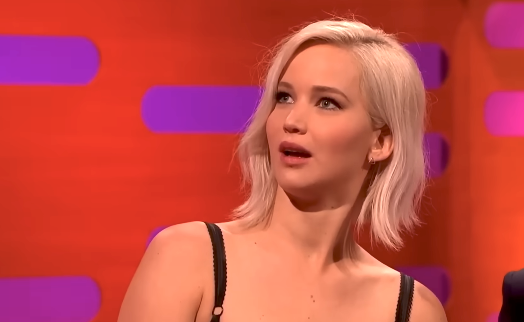 Person with abbreviated hairsbreadth looks amazed during a speech show, wearing a stylish sleeveless top