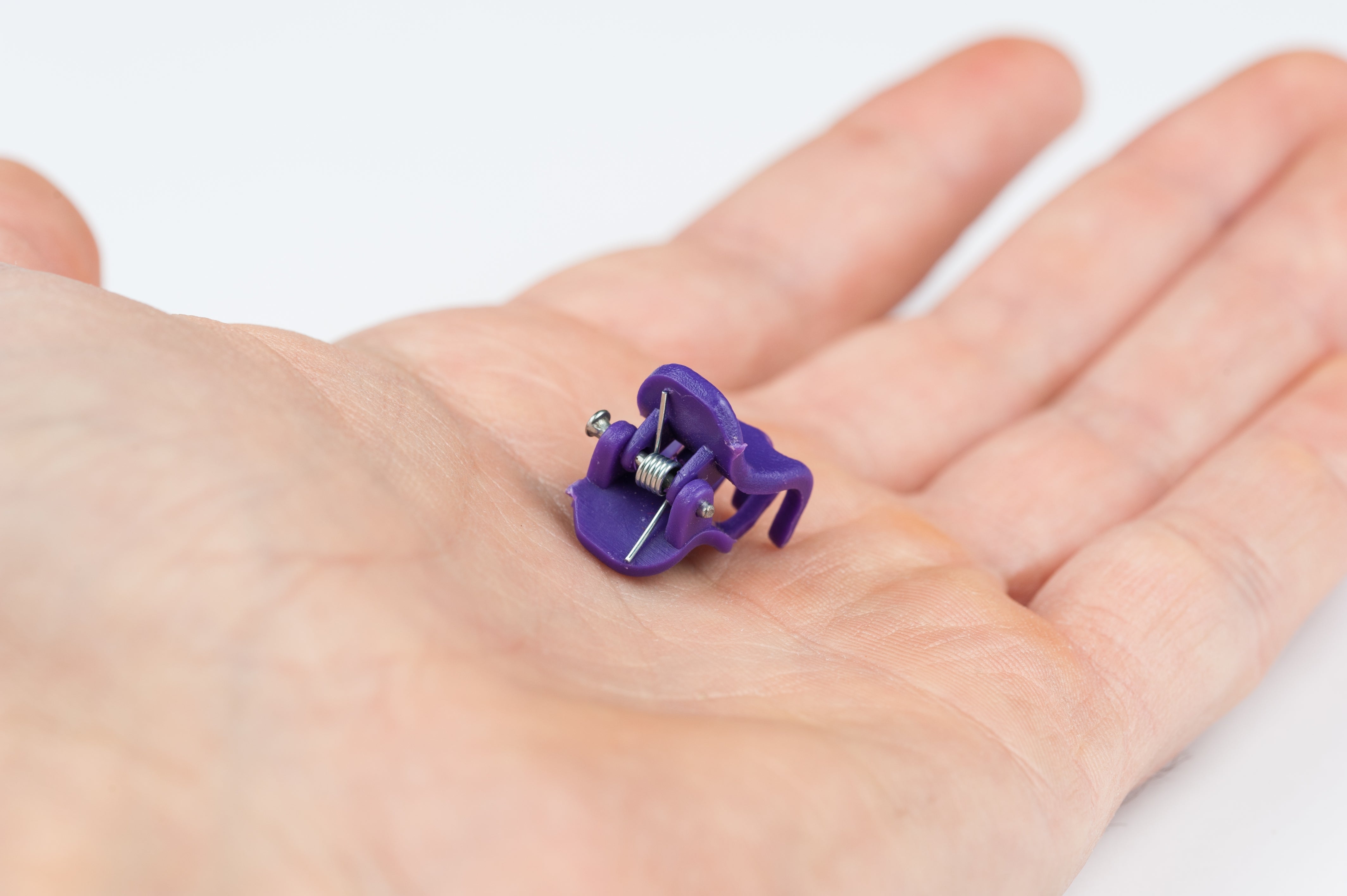 Small purple medical clip resting on a person's open palm, possibly used for health or therapeutic purposes