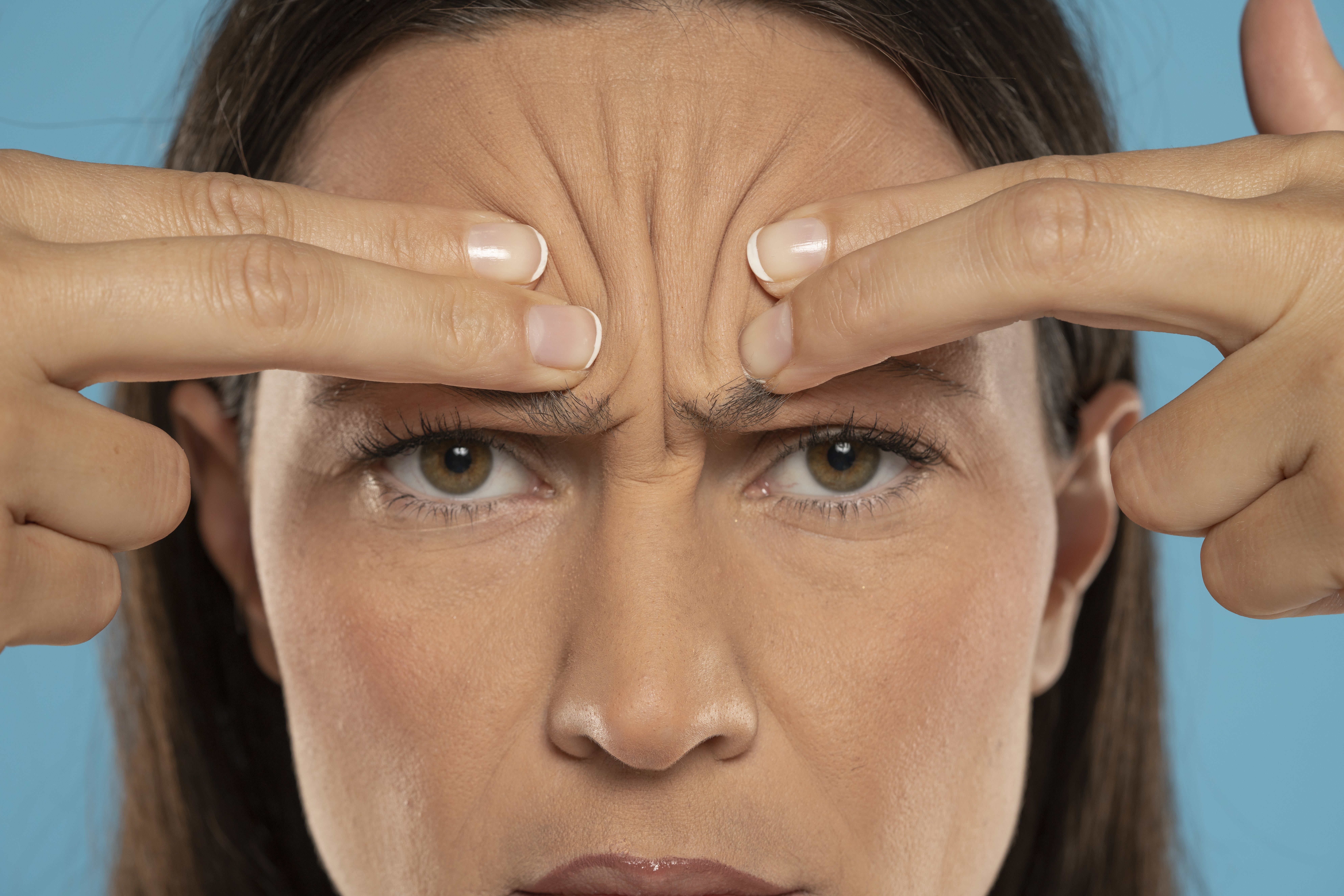 Person pressing their forehead with fingers, focusing on skin and frown lines. Health and skincare focus