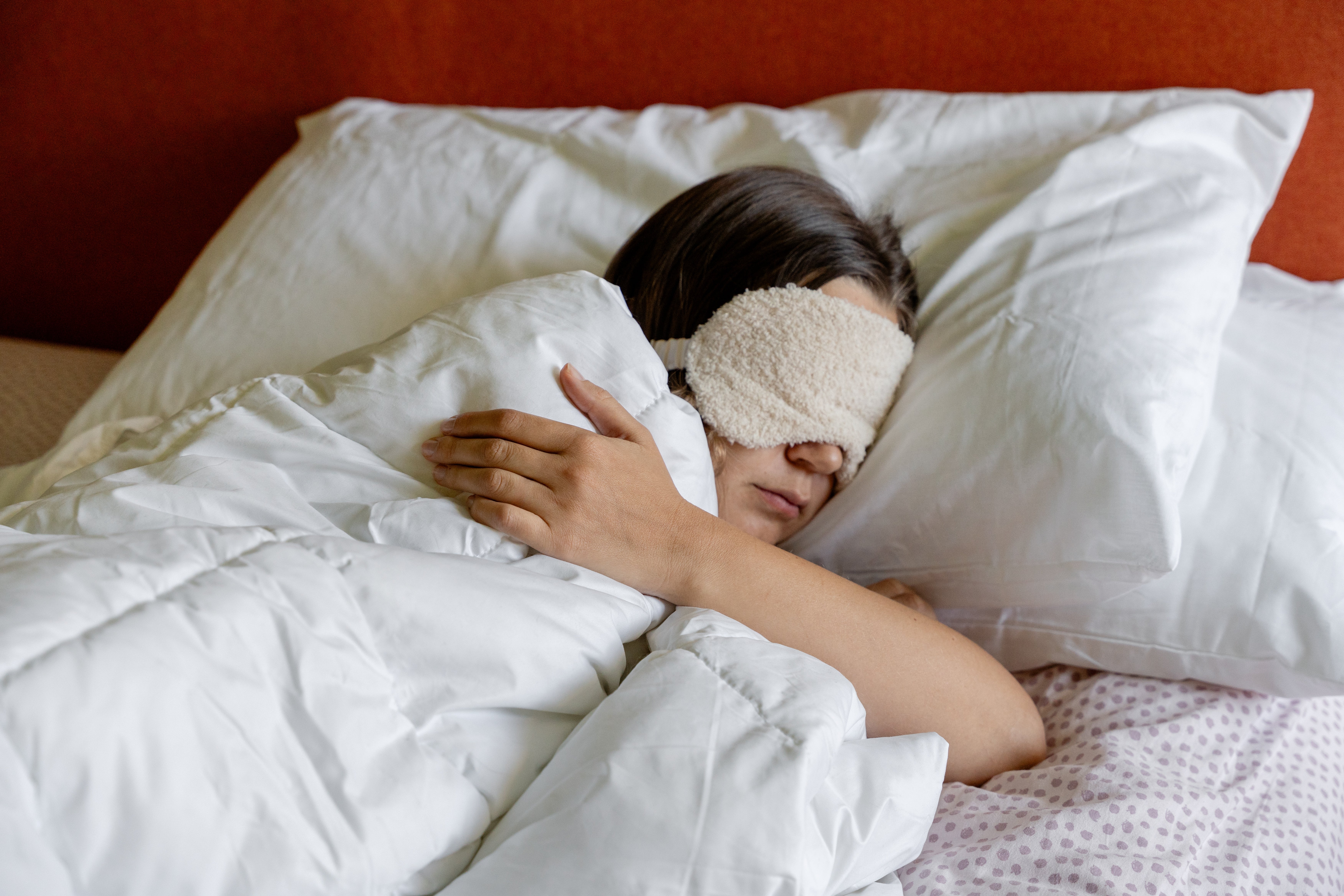 Person sleeping in bed with a sleep mask on, wrapped in a blanket