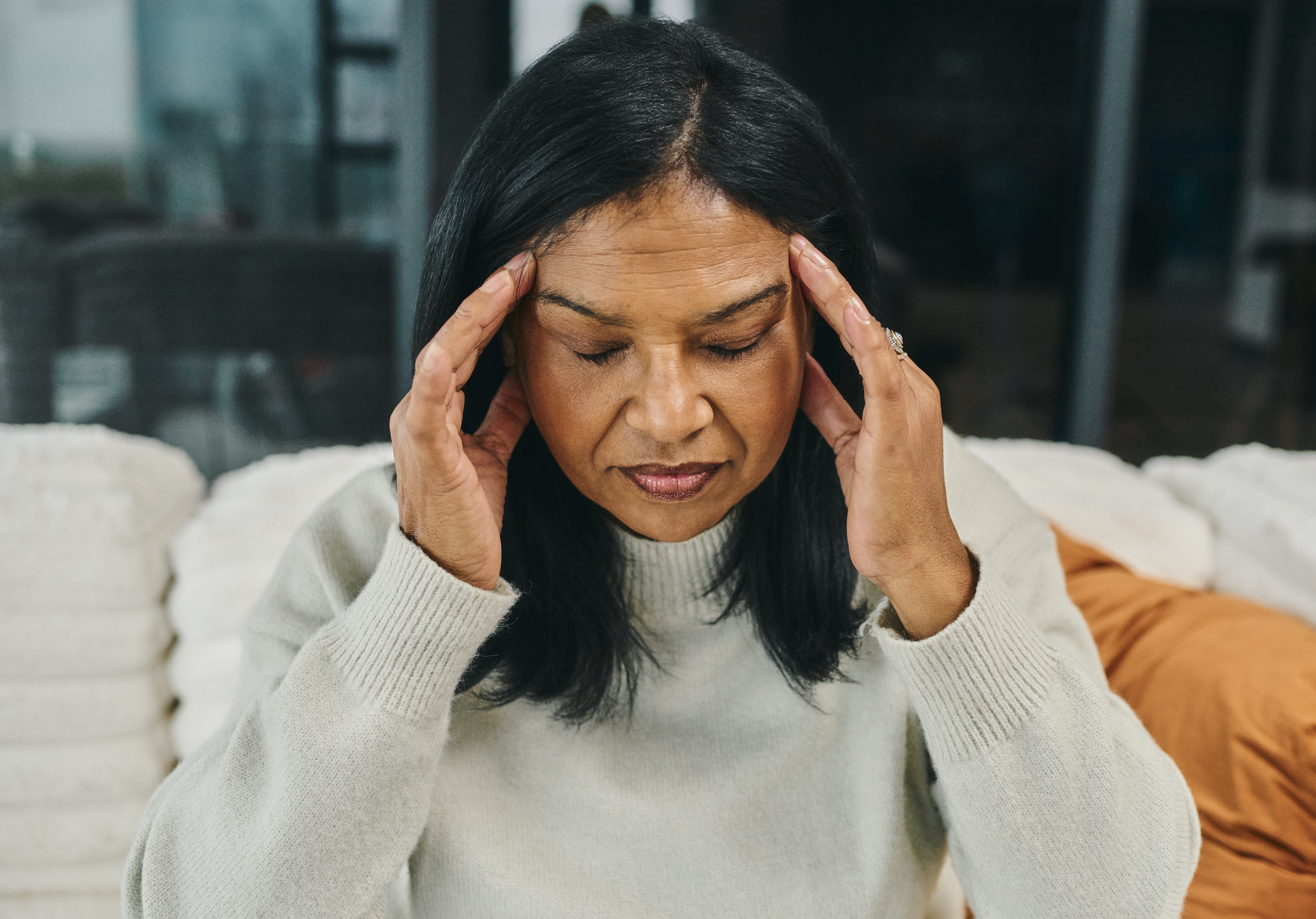 A person sits, holding their head with both hands, appearing to have a headache or be stressed