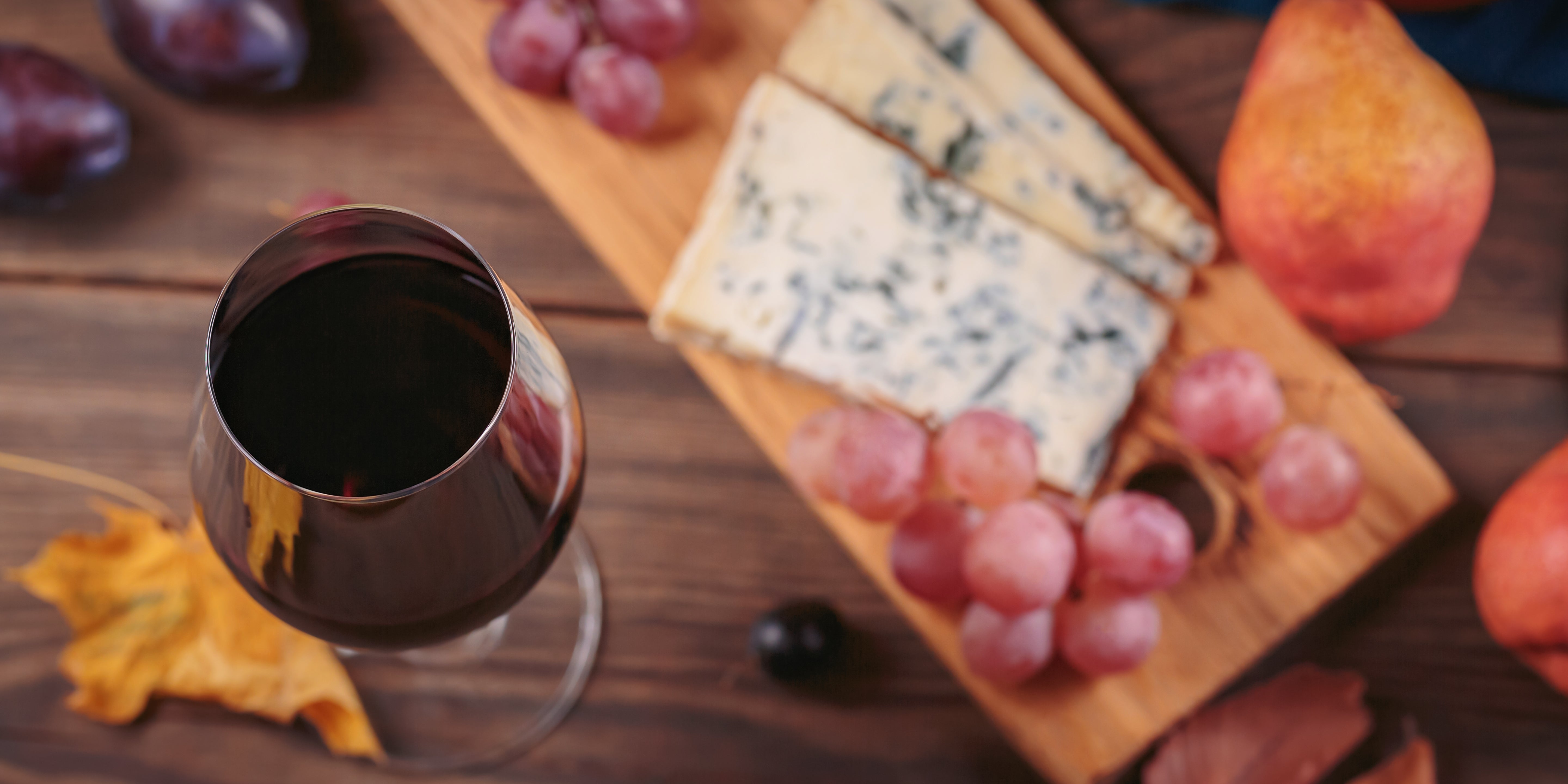 Wine glass with grapes, cheese, and pear on a wooden board, symbolizing a focus on nutrition or balanced diet in a health-themed article