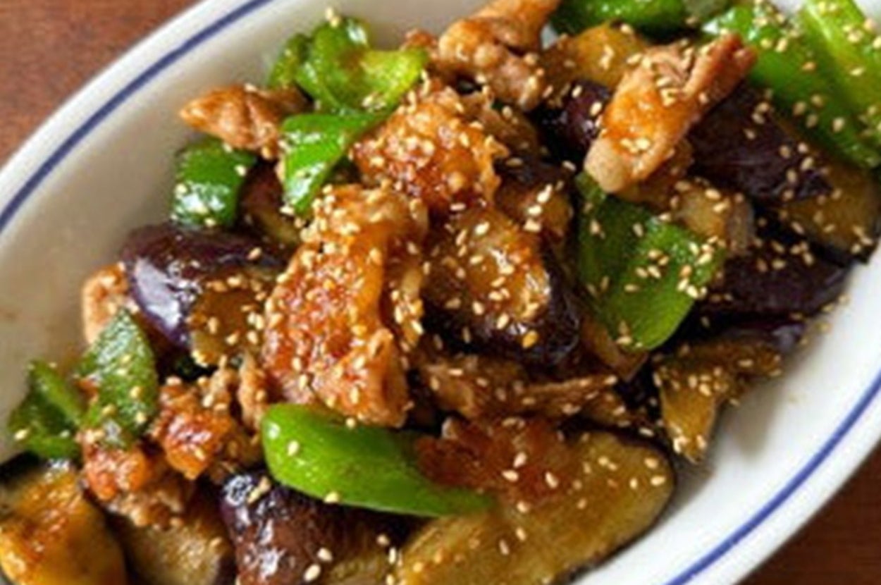 料理が盛り付けられた白い楕円形の皿。なす、ピーマン、鶏肉にゴマがかかっている。