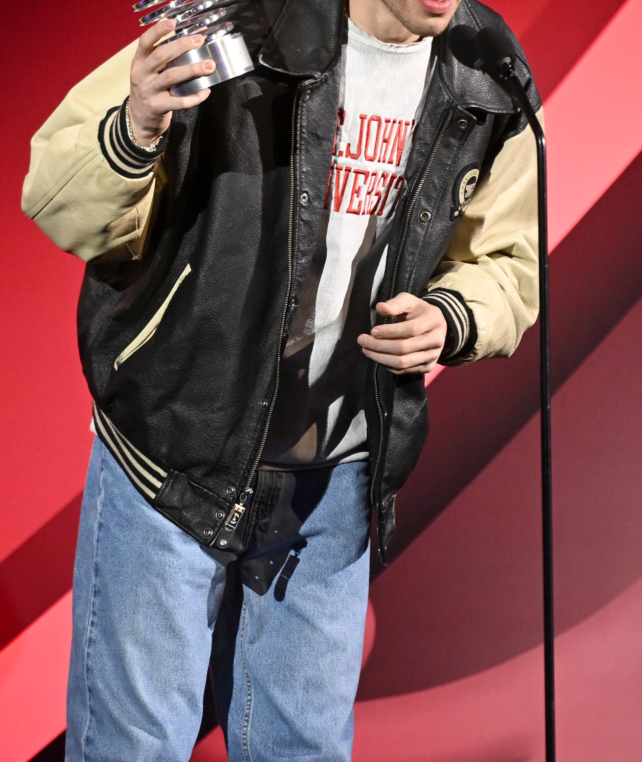 Person in casual varsity jacket and jeans holding an award on stage