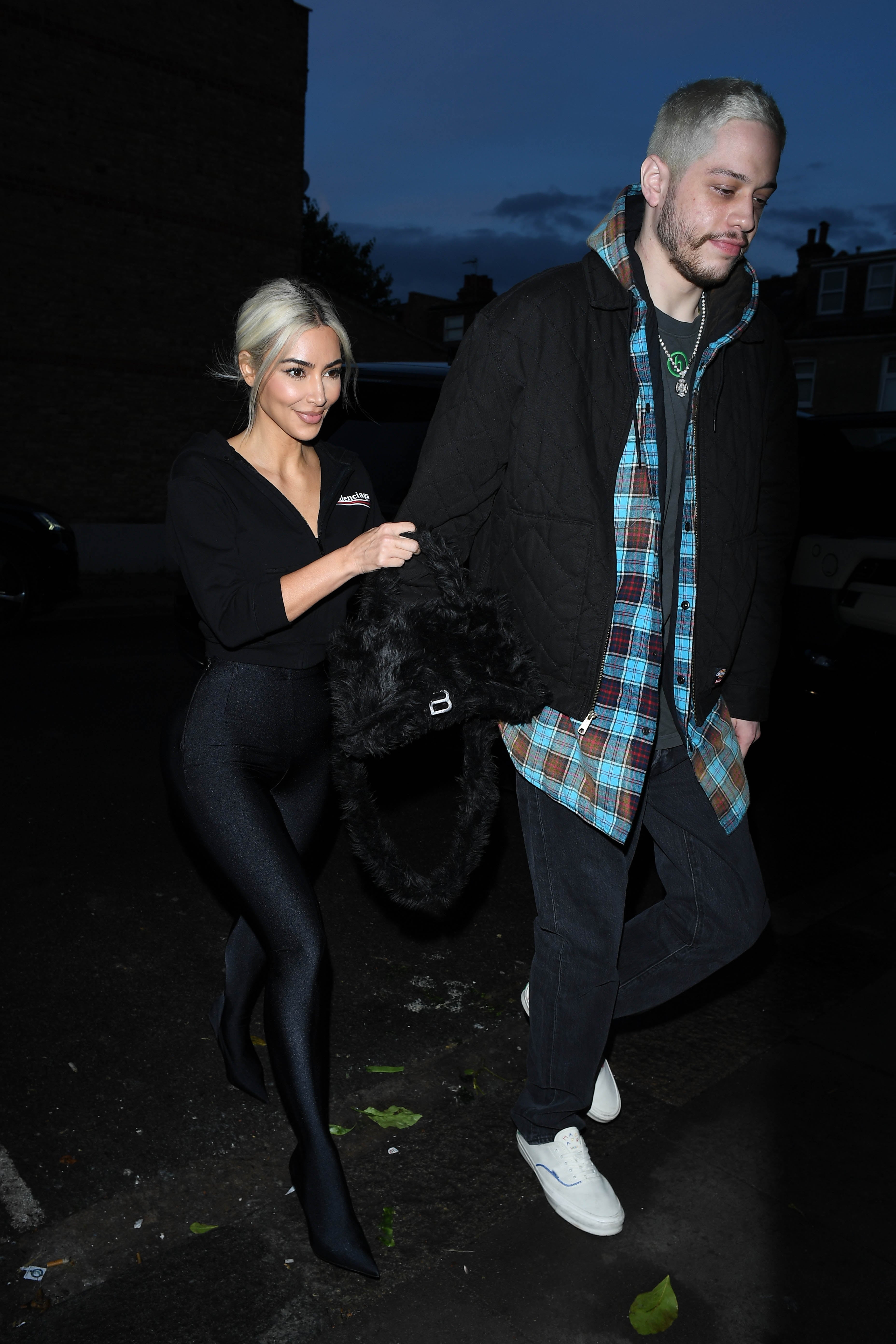 Two people walking; one in a chic outfit, the other in casual wear with a plaid shirt and coat