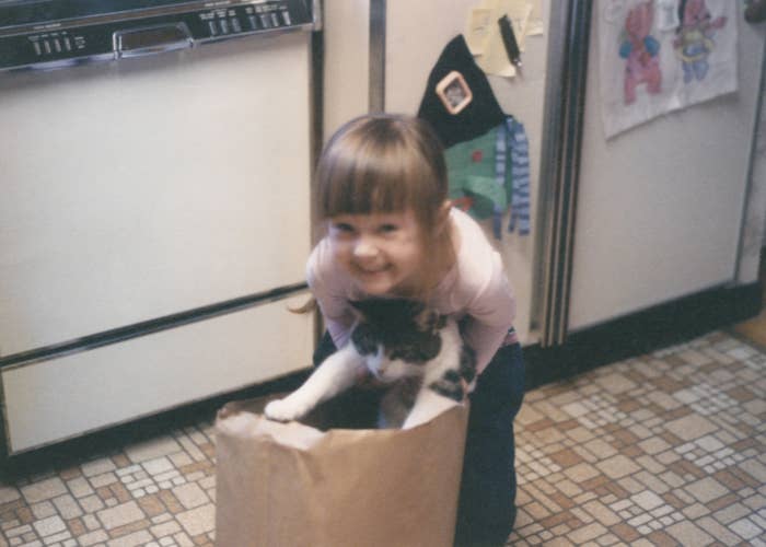 Child happily holding a black and white cat in a paper bag on a kitchen floor