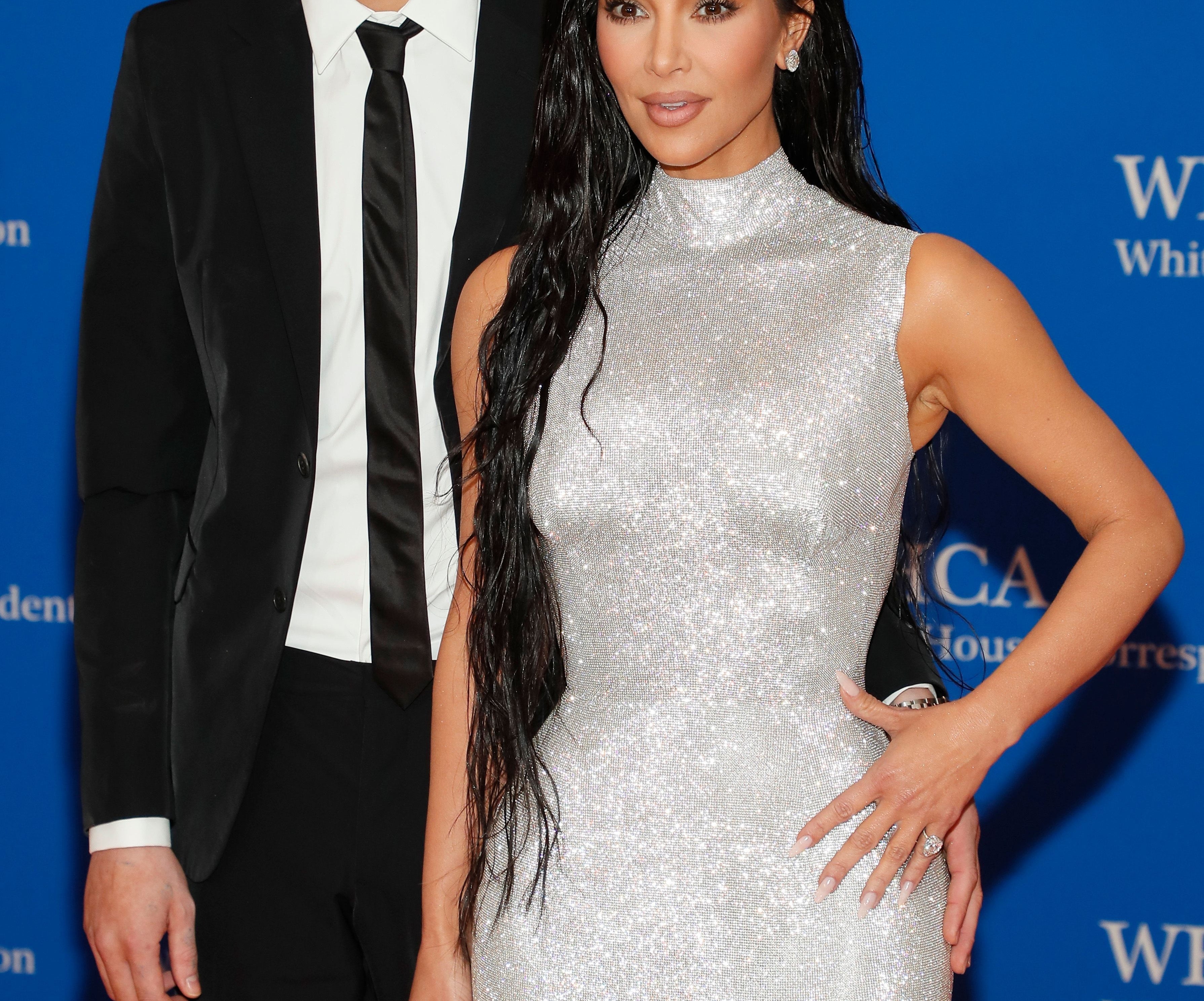 Two individuals at a formal event. One wears a suit with sunglasses, the other in a shimmering, fitted evening gown