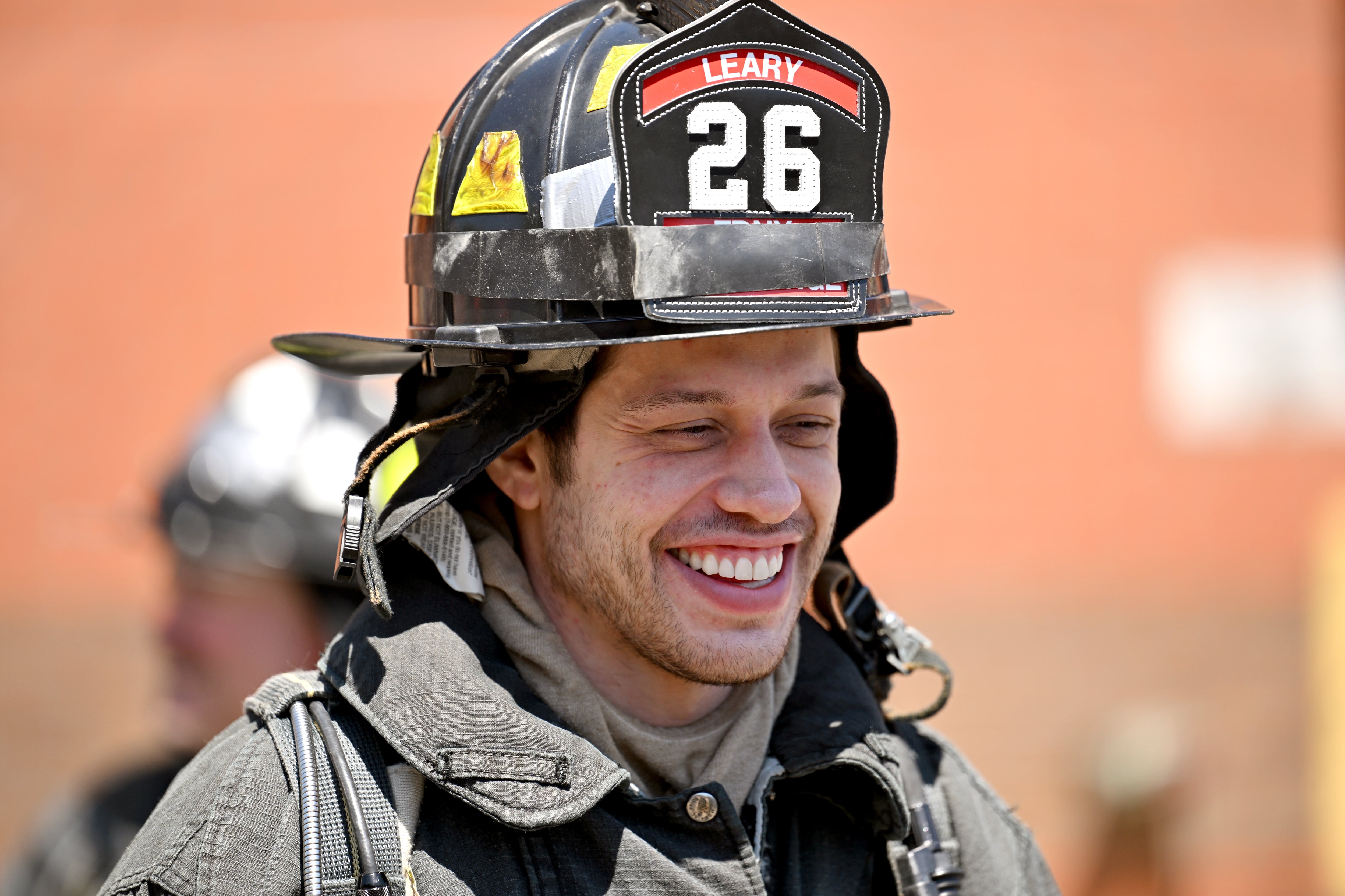 Person wearing a firefighter's uniform and helmet with "Leary 26" on it, smiling