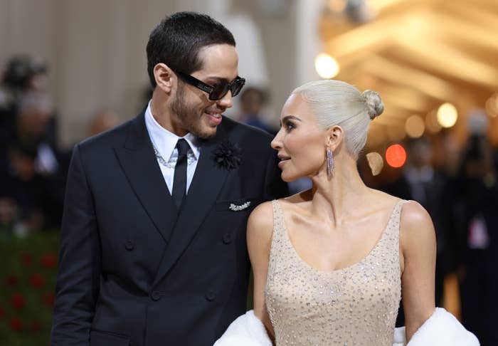 A couple on a red carpet event, with one person wearing a suit and the other in a sparkling gown and earrings, both looking at each other
