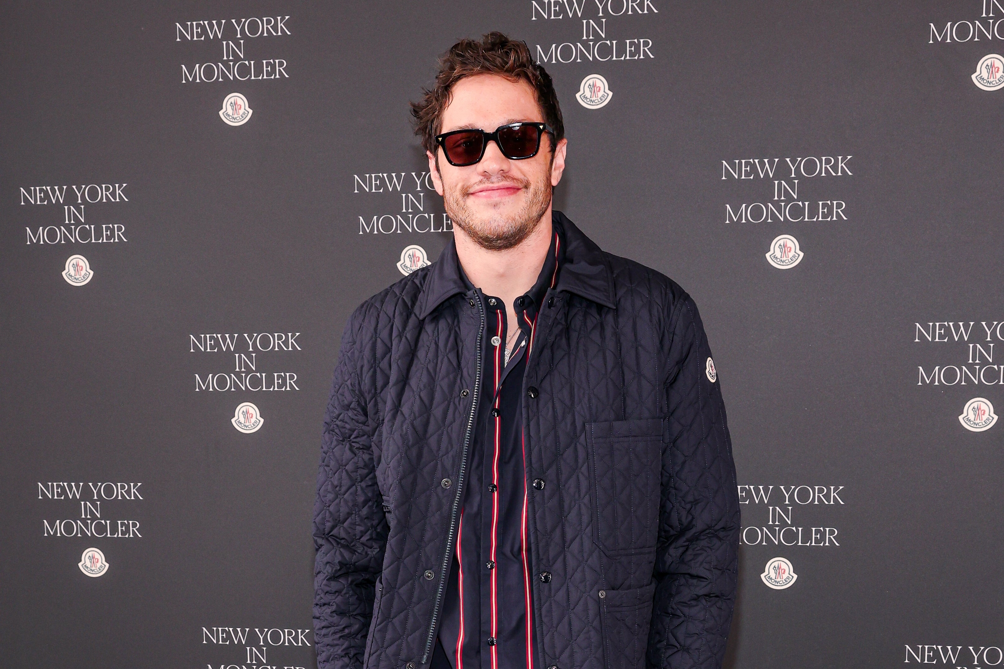 Person in a quilted jacket and sunglasses at a "New York in Moncler" event backdrop