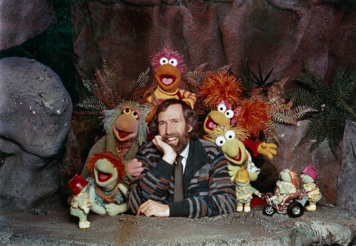 Jim Henson with Fraggle Rock muppets successful  a grotto setting, smiling and surrounded by colorful puppet characters