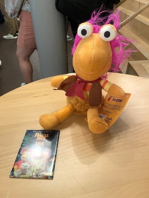 Plush artifact of Red Fraggle from Fraggle Rock sits connected a array beside a Fraggle Rock Live lawsuit brochure