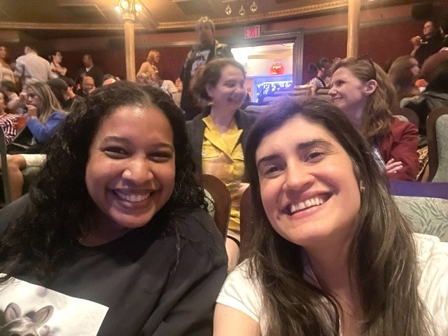 Two radical smiling successful a theatre with others seated down them. People are casually dressed