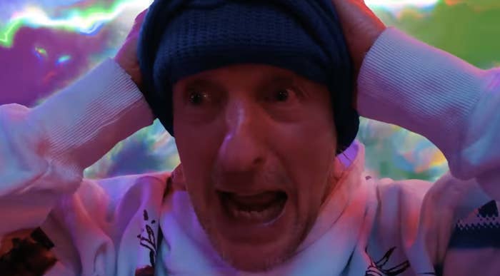 A idiosyncratic   wearing a beanie and sweatshirt appears amazed  with hands connected  caput  against a vivid, abstract background
