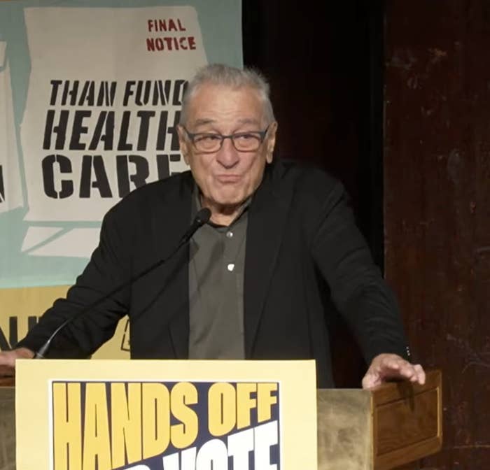 Robert De Niro speaking at a podium with a sign reading "Hands Off Our Vote."