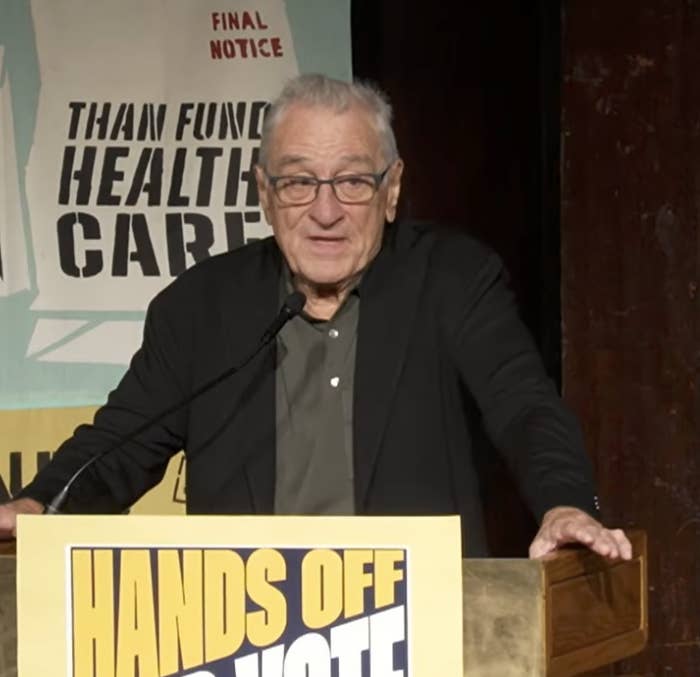 Robert De Niro speaking at a podium with a sign reading "Hands Off Our Vote."