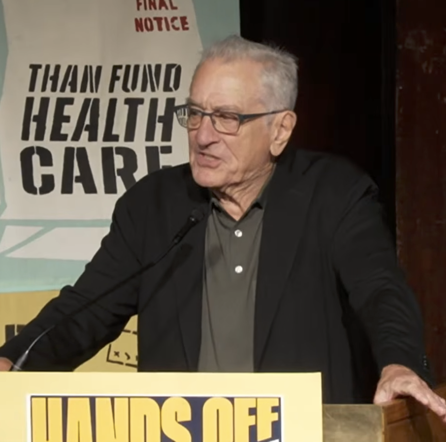 Robert De Niro in a blazer speaking at a podium