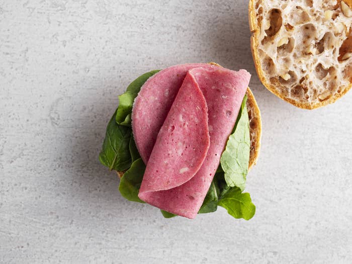 Open sandwich with sliced deli meat on greens, a textured bread top nearby, on a concrete surface