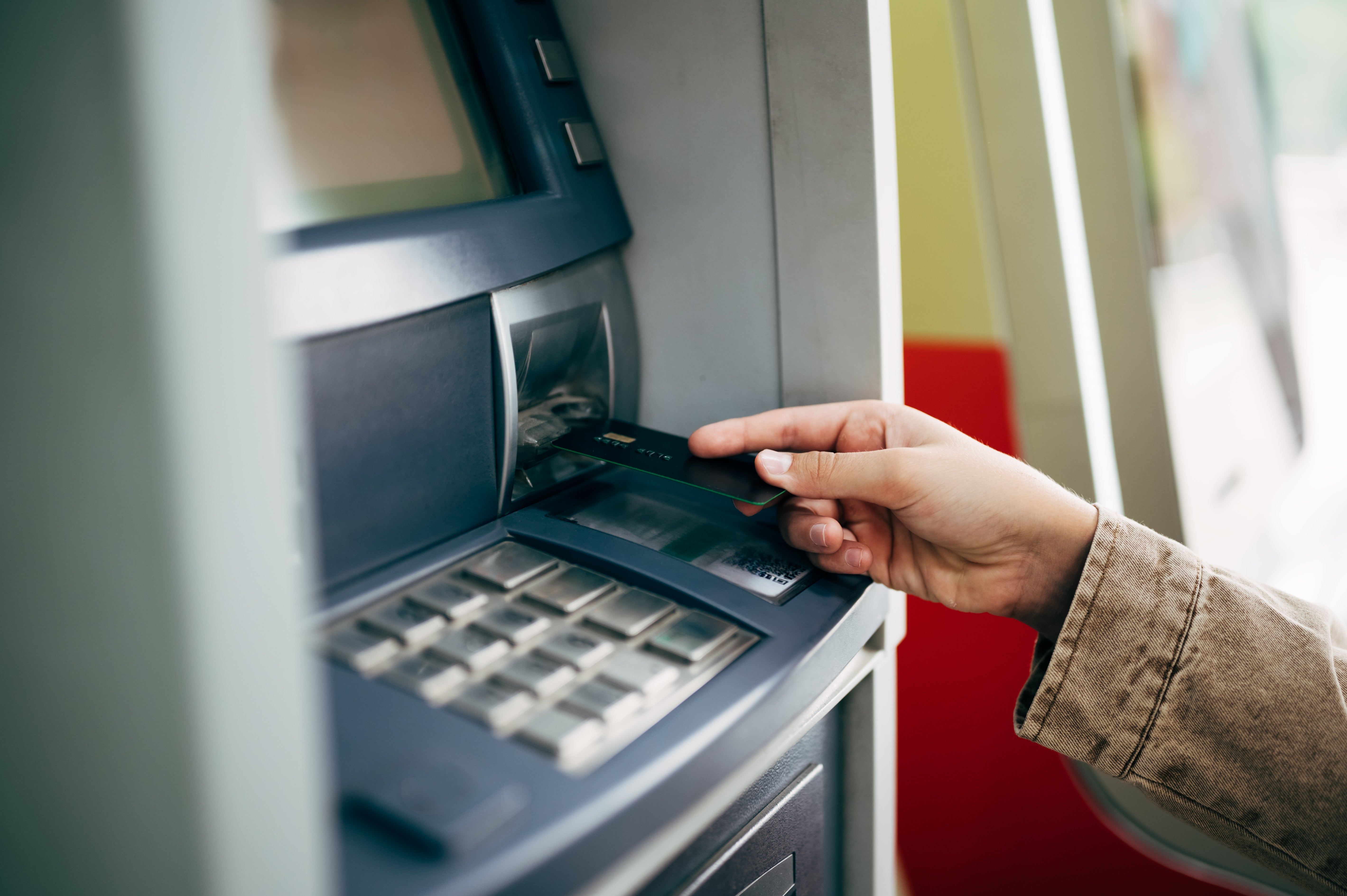 Person using an ATM, inserting a bank card into the machine for a transaction