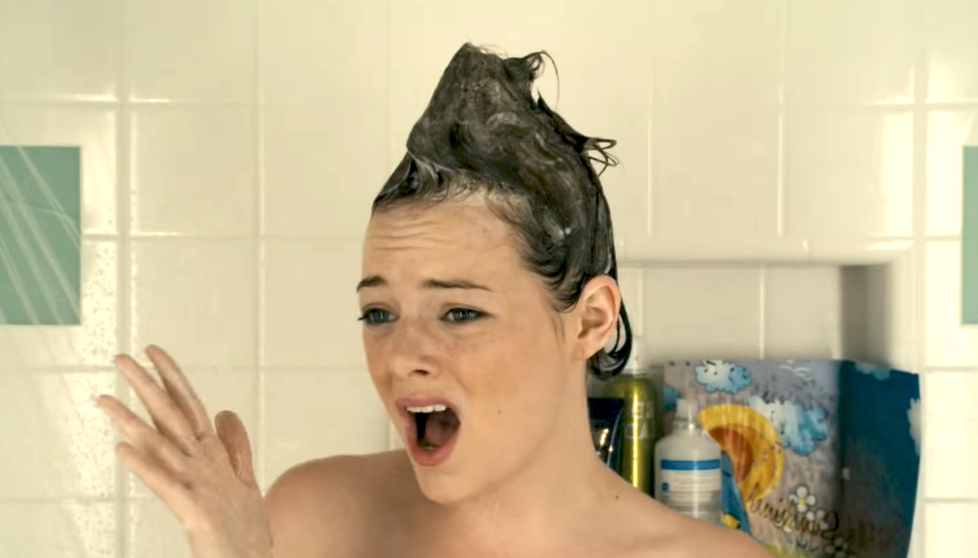 Person in a shower with shampoo in their hair shaped into a peak, showing a surprised expression